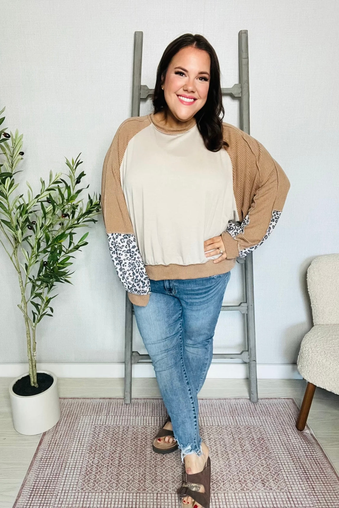 Smiling woman wearing beige and camel dolman colorblock terry top with leopard print sleeve accents and jeans indoors