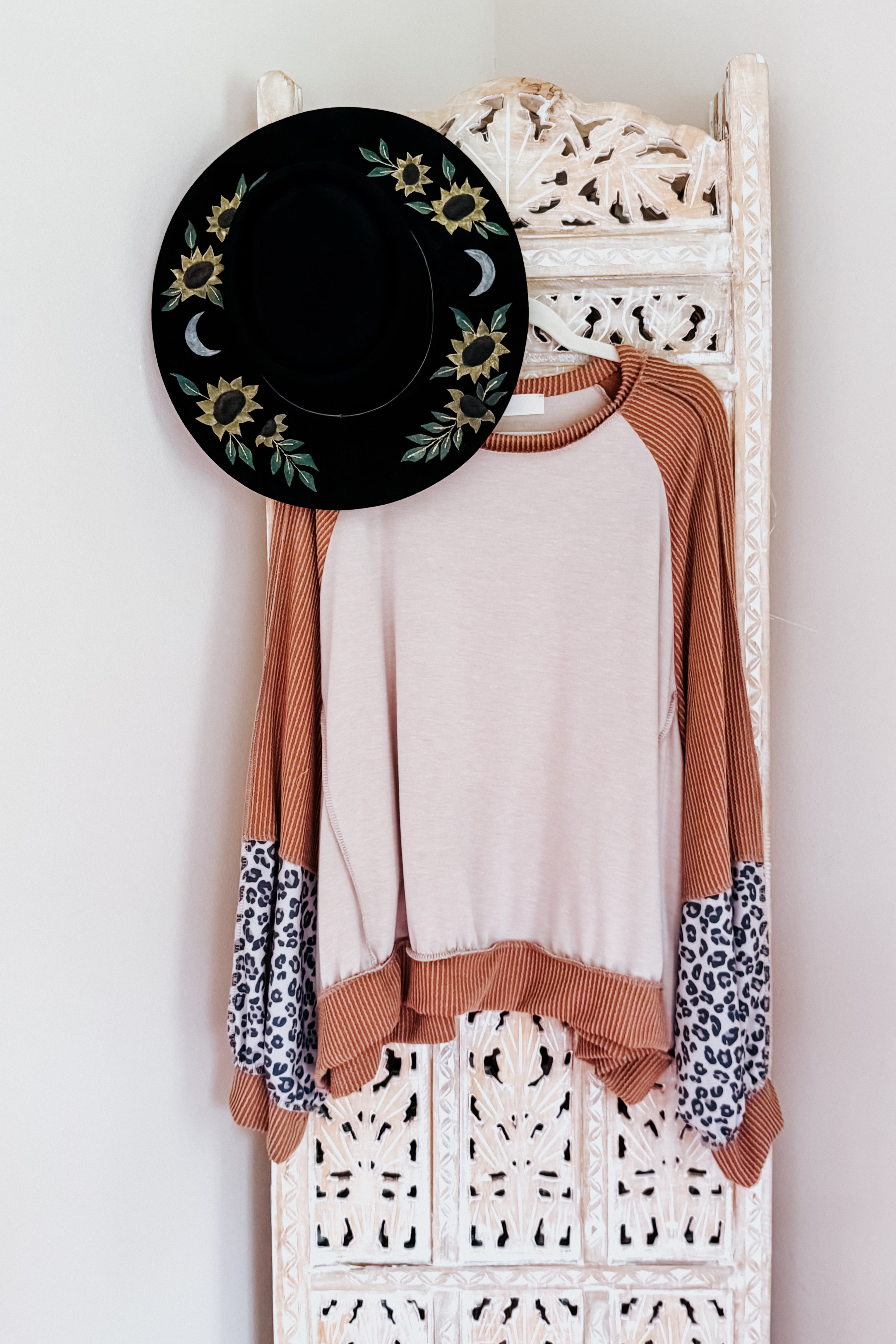 Raglan sleeve colorblock terry top with rust orange, light pink, and leopard print panels hanging next to black floral hat