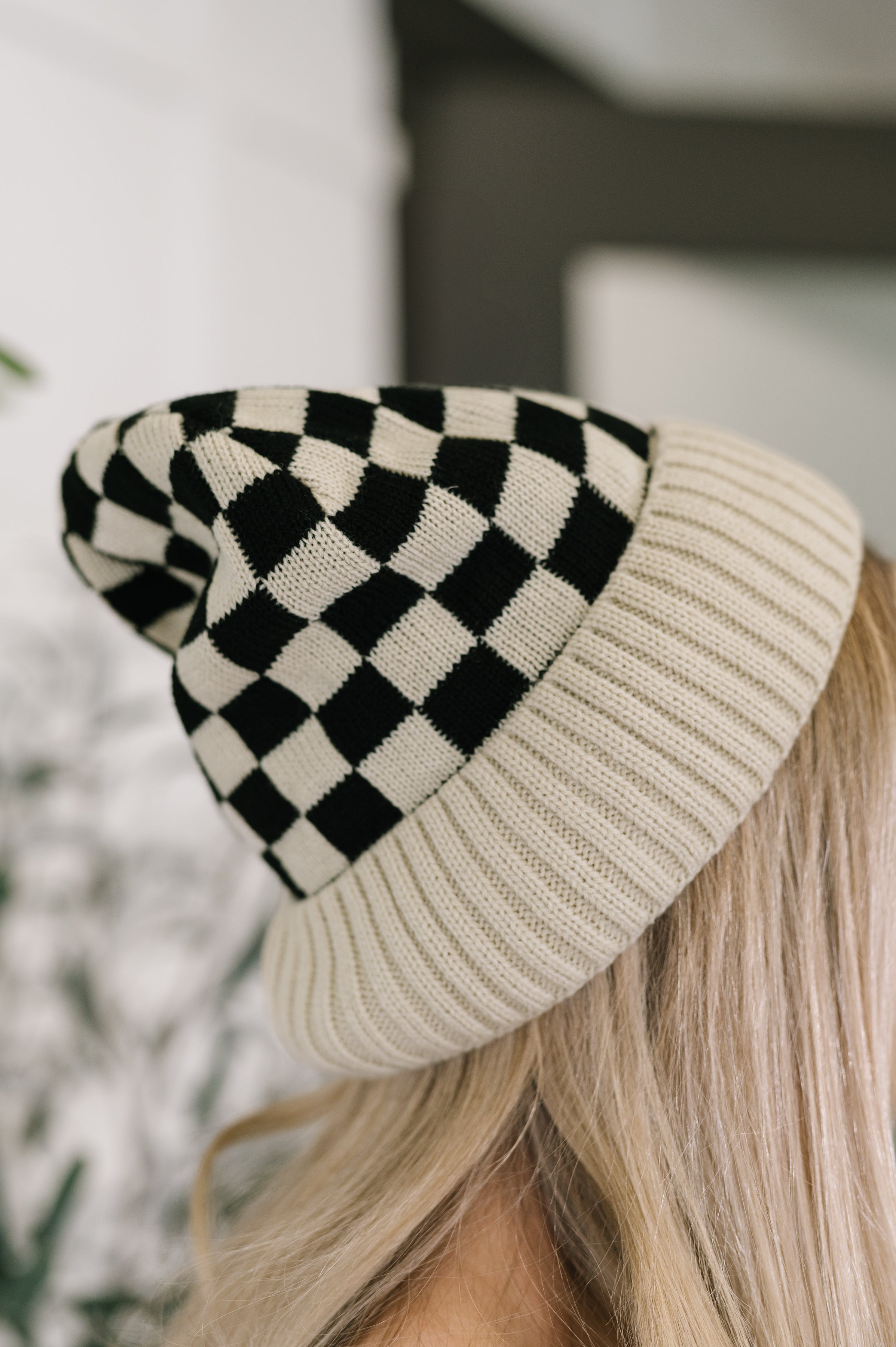 Close-up of a bone-colored ribbed beanie with black checkerboard pattern worn by a person with blonde hair