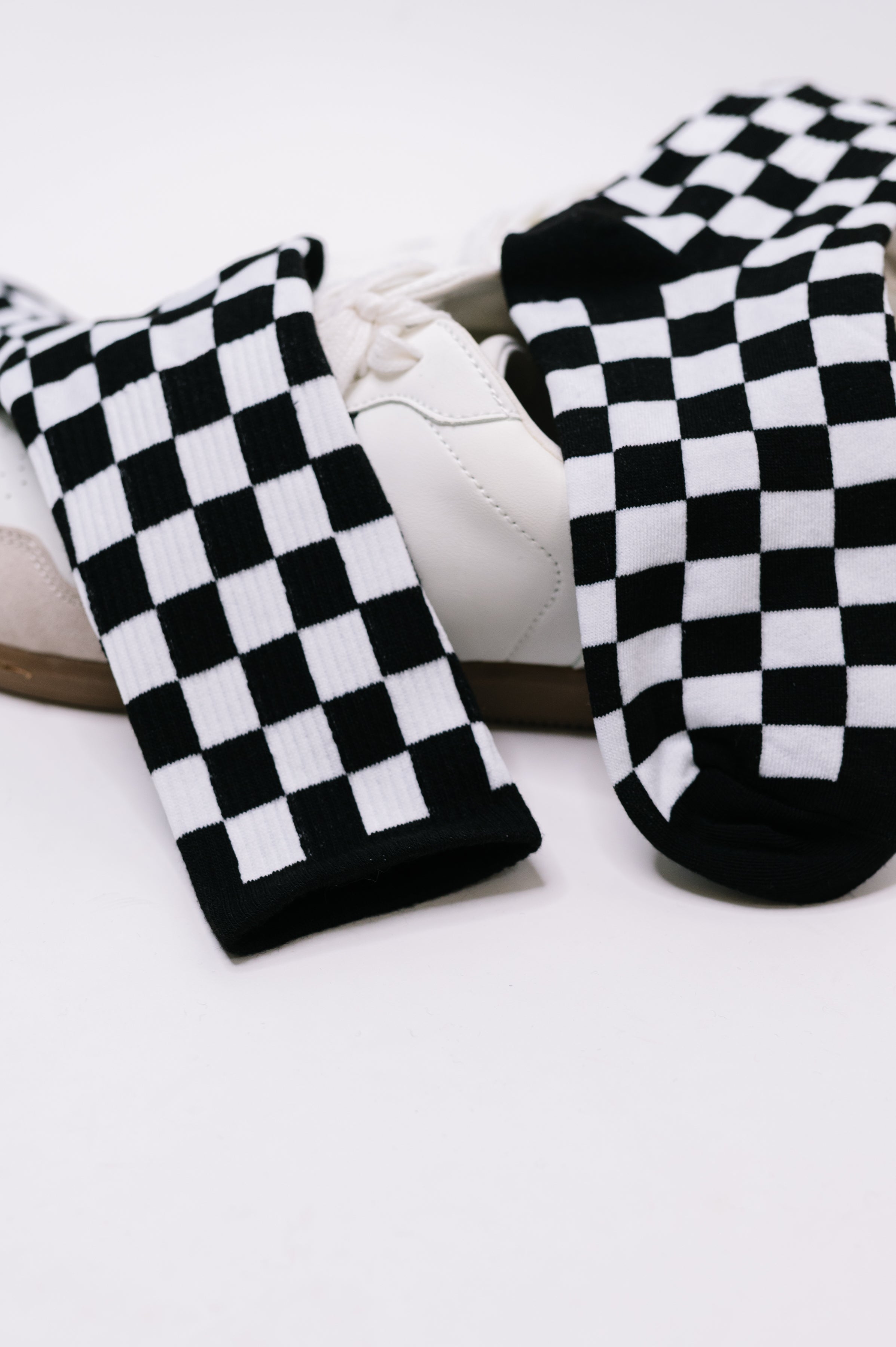 Black and white checkered quarter socks draped over white lace-up sneakers on white background