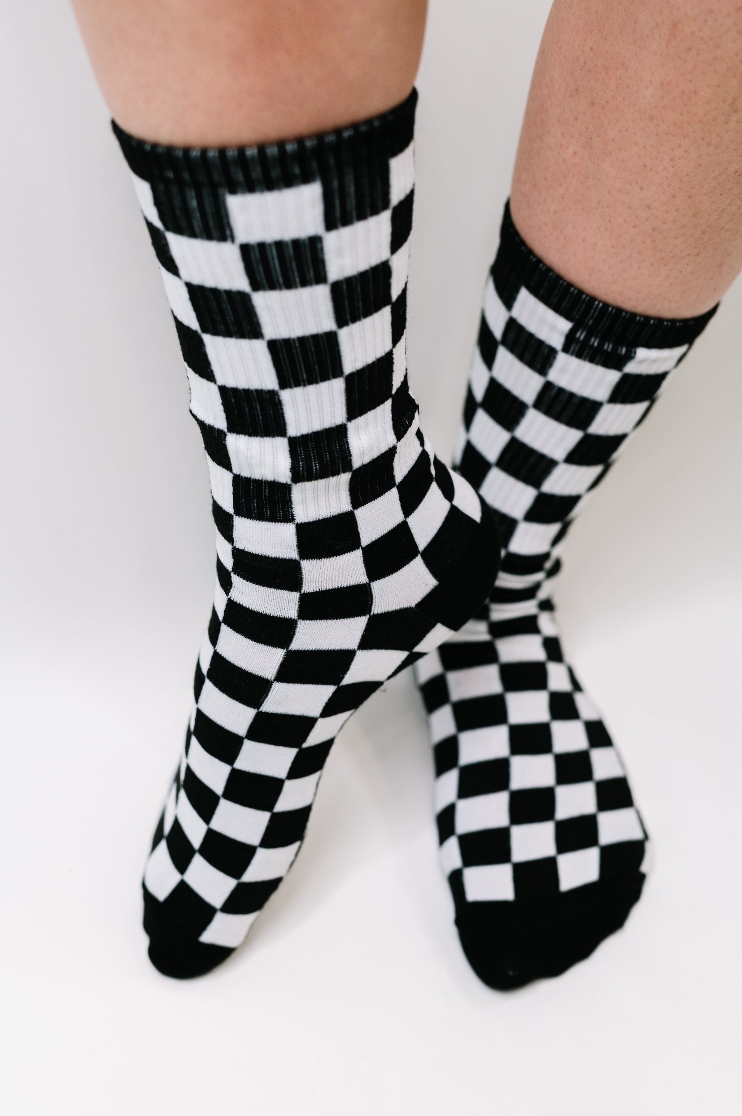 Close-up of legs wearing black and white checkered quarter length socks with ribbed cuffs on white background