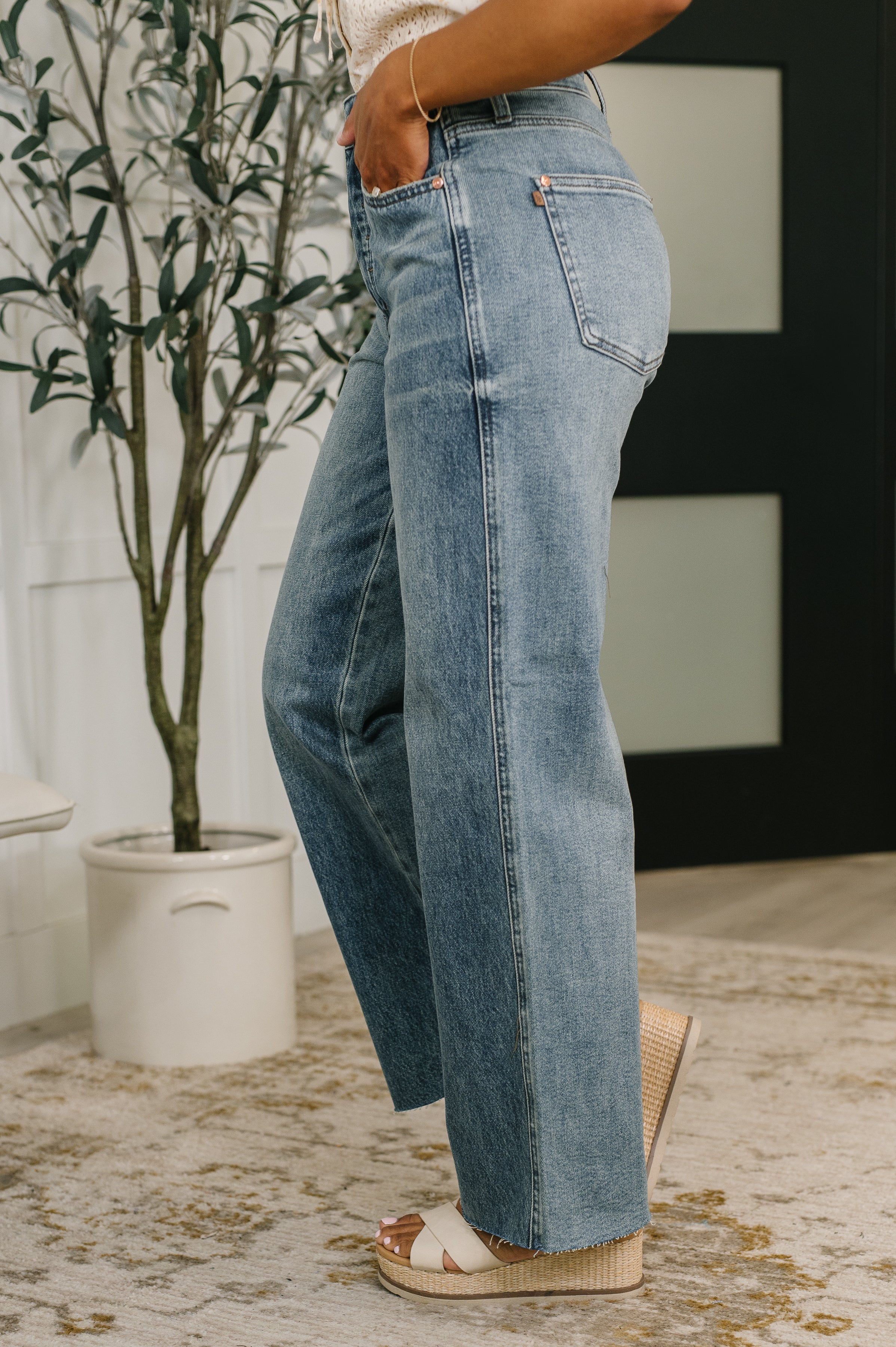 Side view of blue high waist baggy jeans paired with white wedge sandals on a textured rug indoors