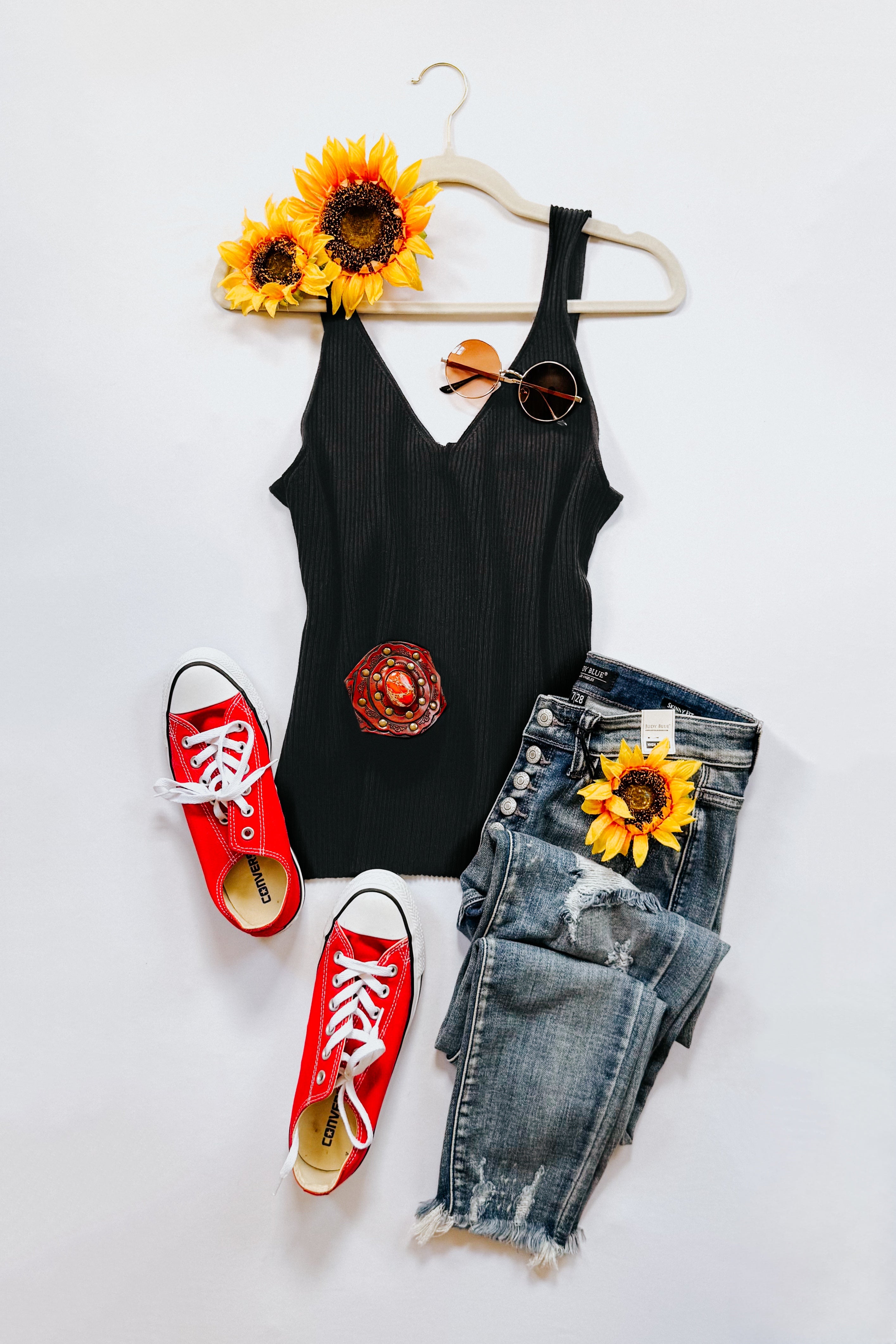 Black ribbed tank top paired with distressed blue jeans and red low-top sneakers styled with sunflowers and sunglasses
