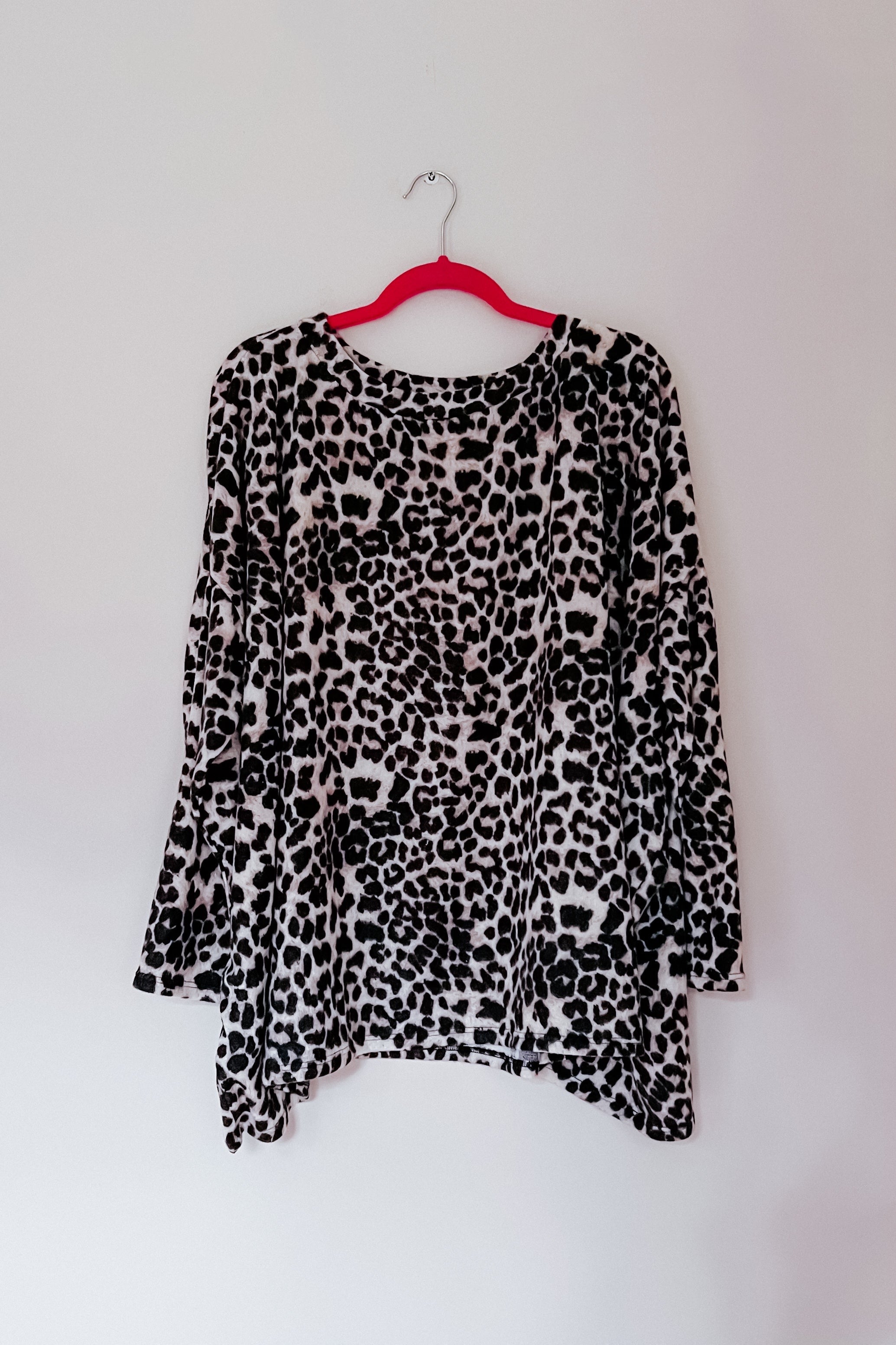 Black and white animal print long sleeve top with relaxed fit hanging on red hanger against plain wall