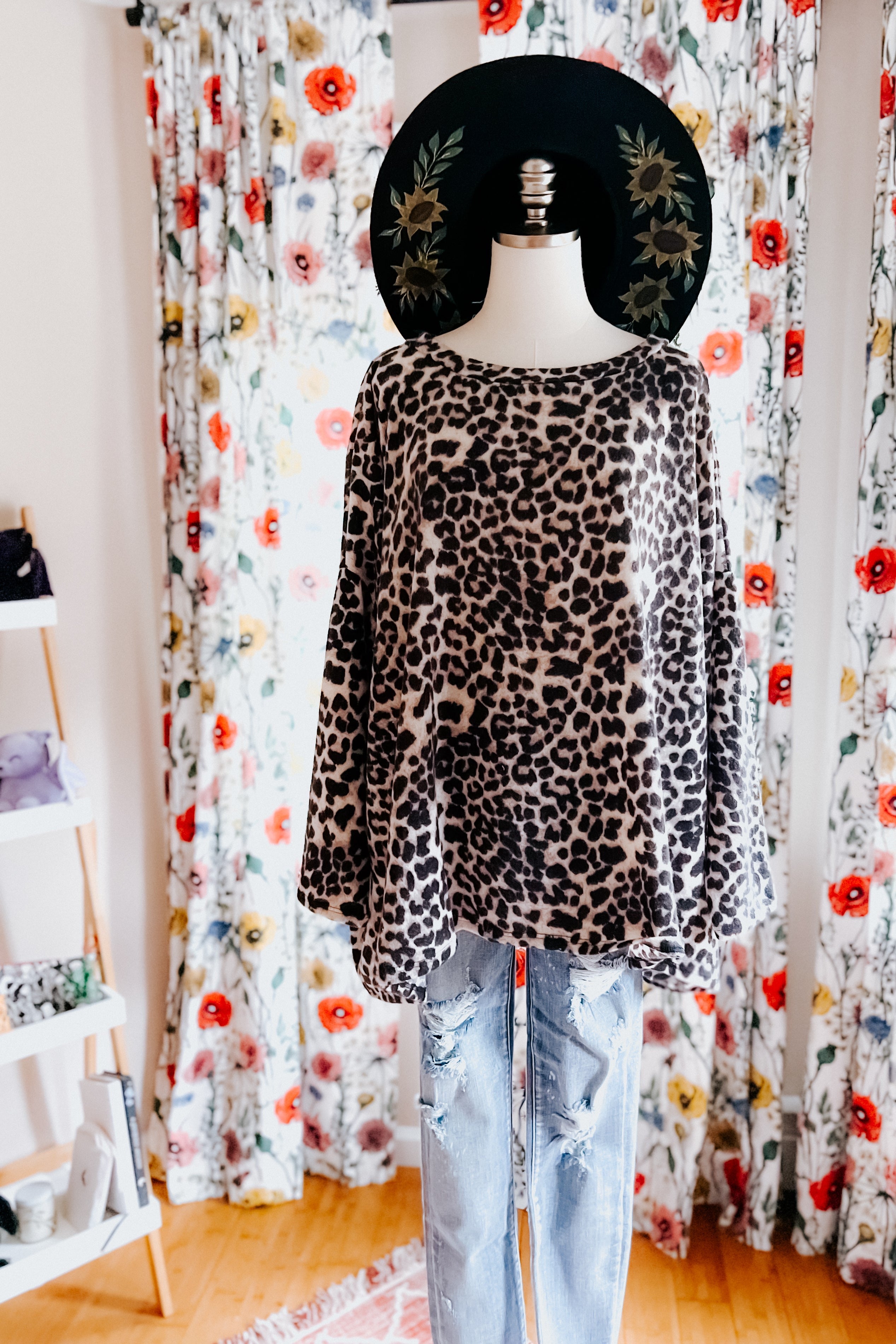 Leopard print long sleeve top displayed on mannequin with distressed light blue jeans and floral curtains background