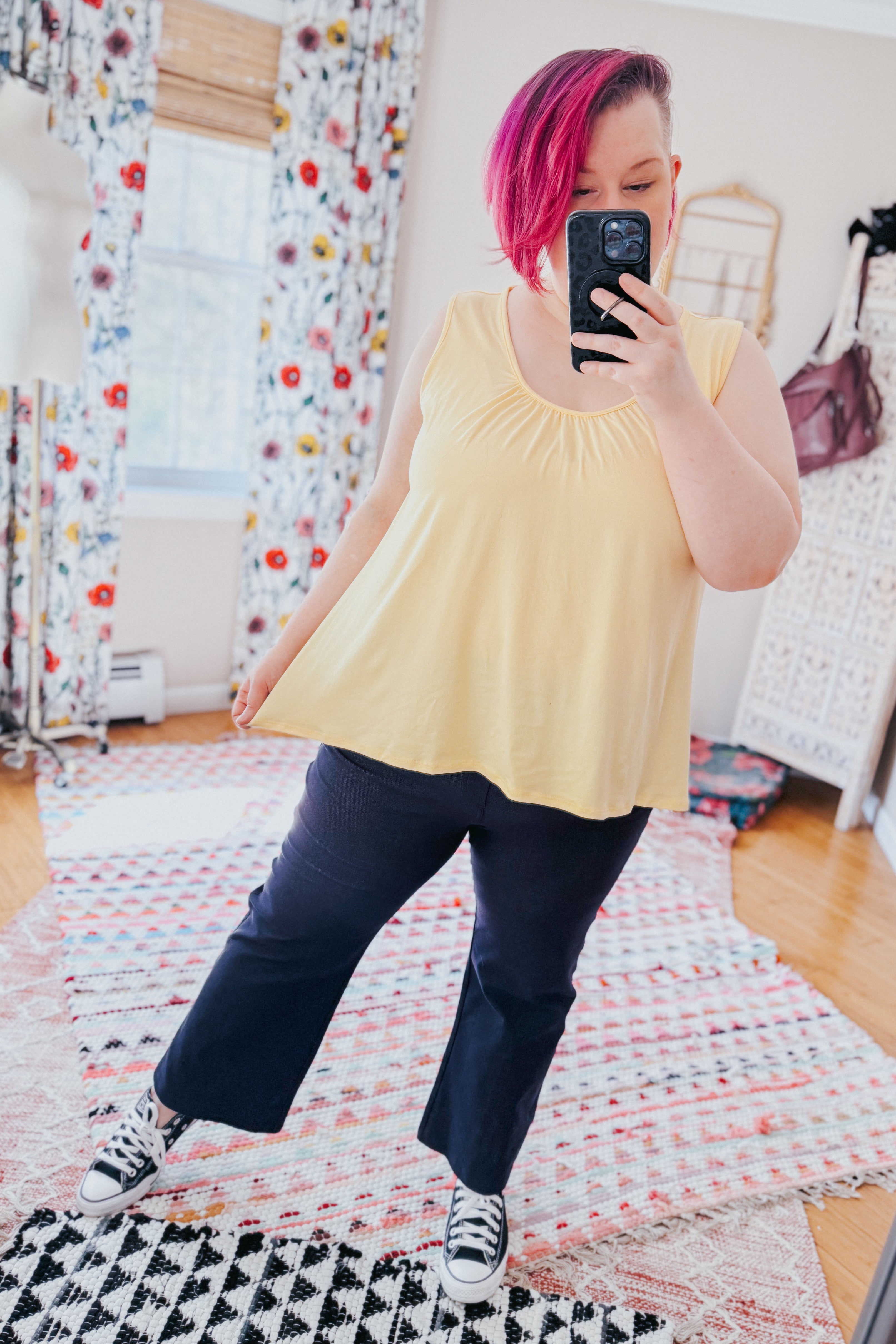 Woman with short pink hair wearing sleeveless yellow top and navy Classic Charm Cropped Pants taking selfie indoors
