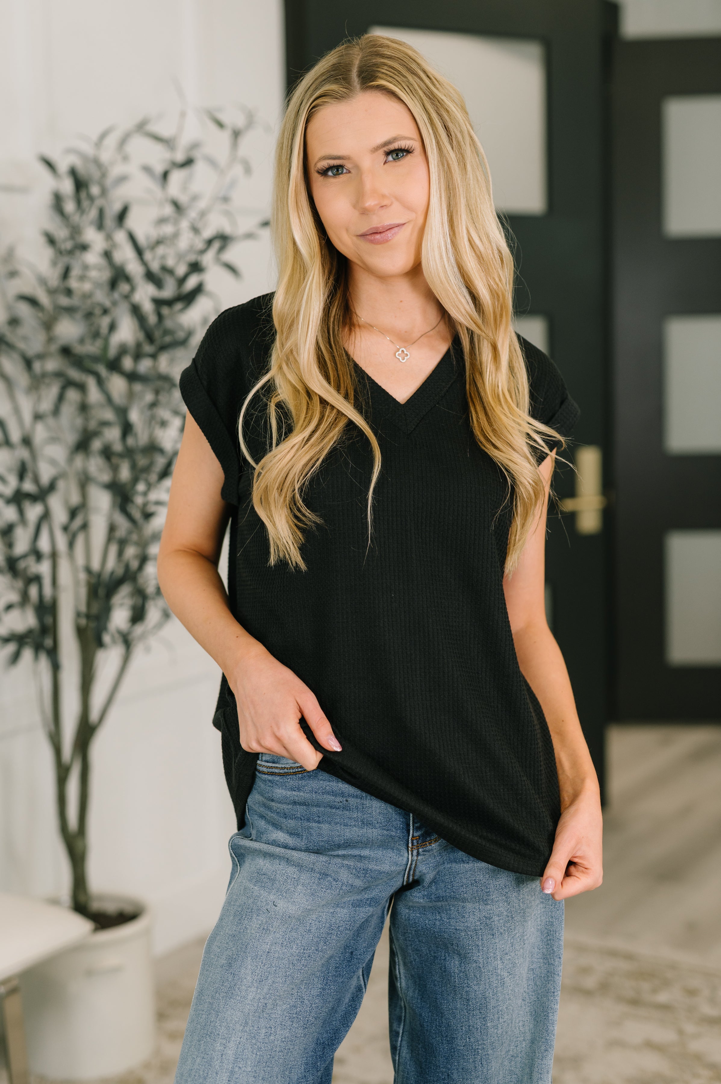 Woman wearing black V-neck tee with rolled sleeves paired with light wash jeans in modern indoor setting
