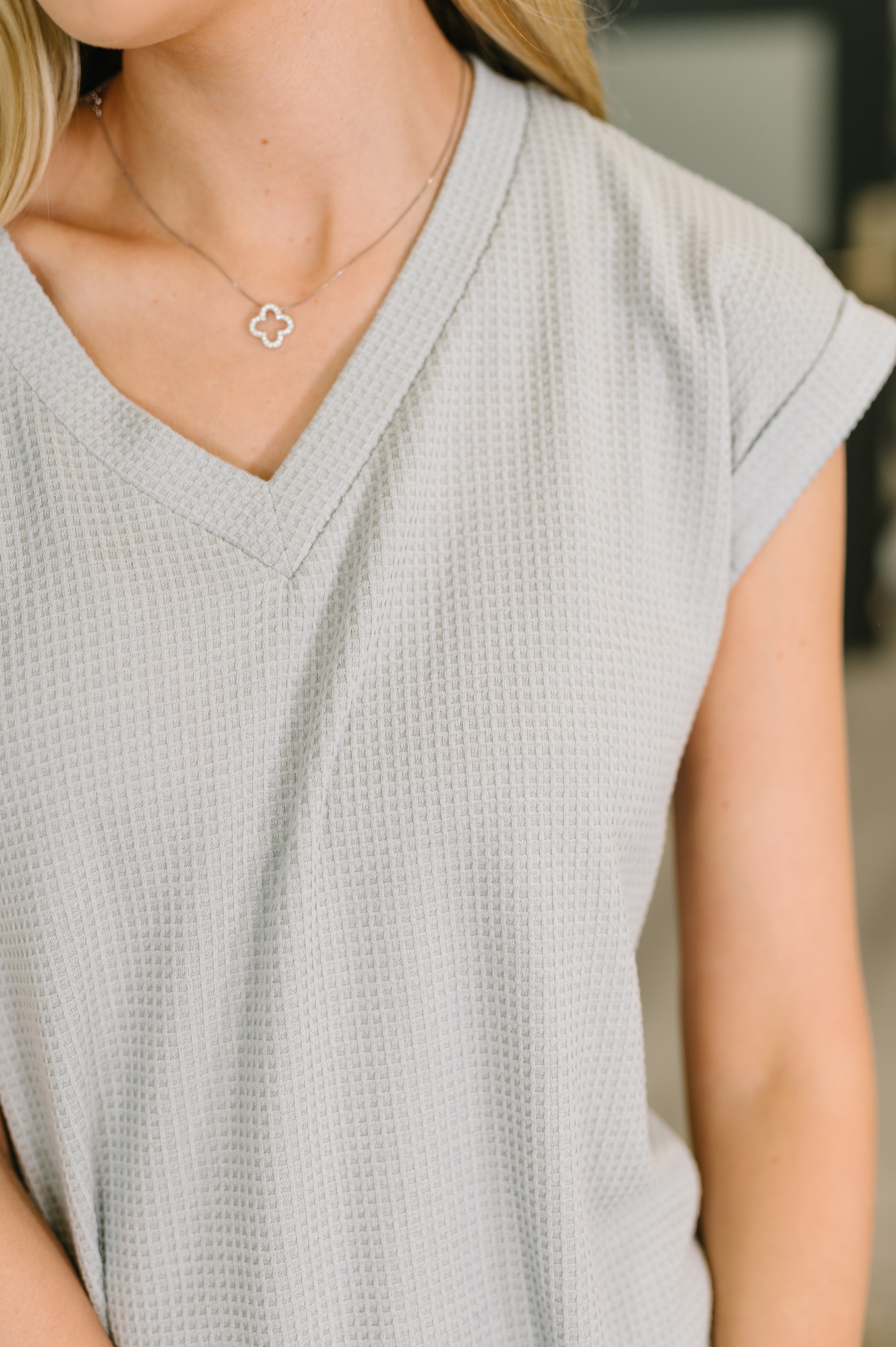 Close-up of woman wearing pearl grey textured V-neck tee with short sleeves and delicate silver clover necklace