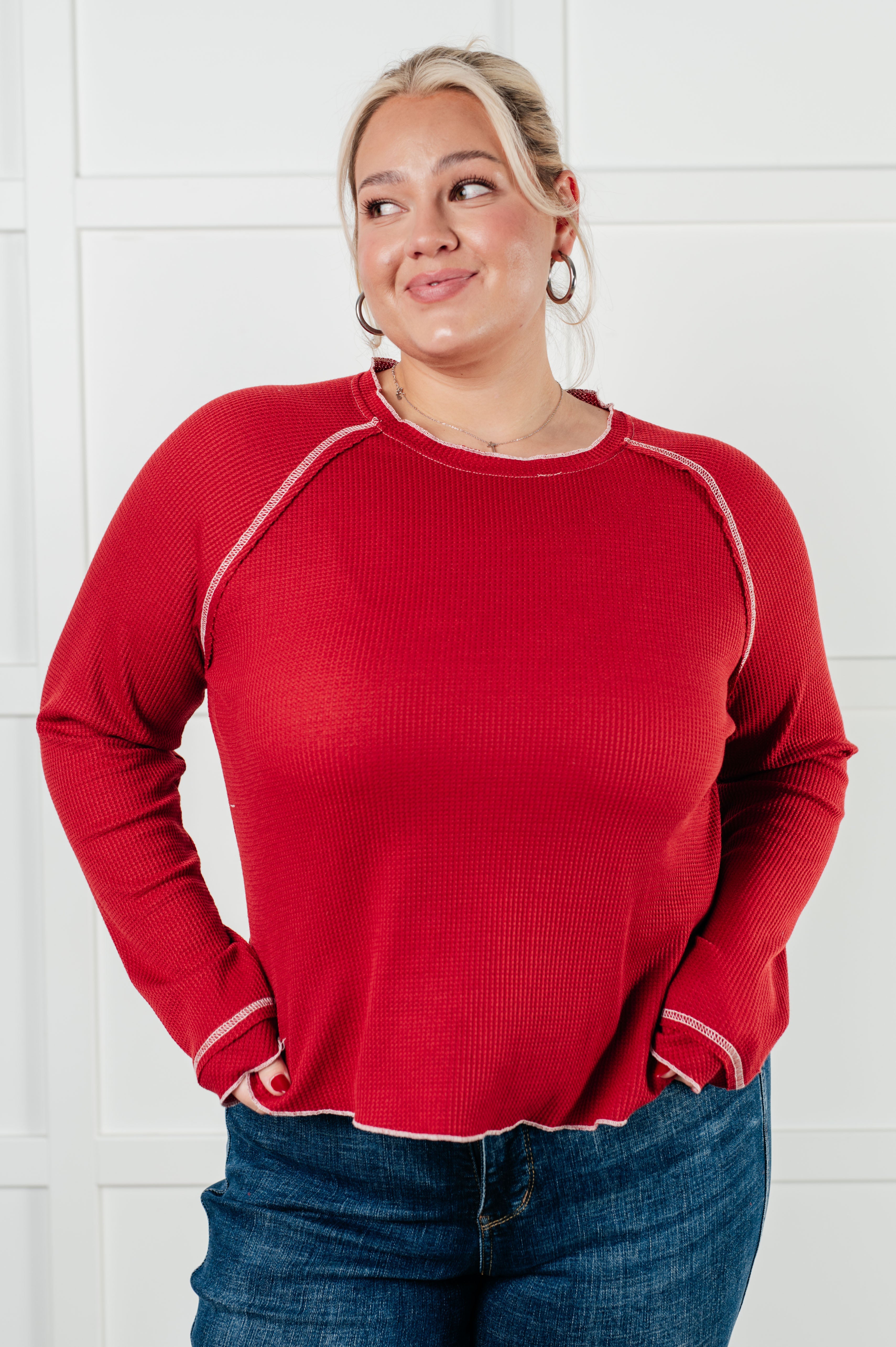 Plus-size woman wearing a red waffle-knit long sleeve top with exposed stitching and dark blue jeans indoors
