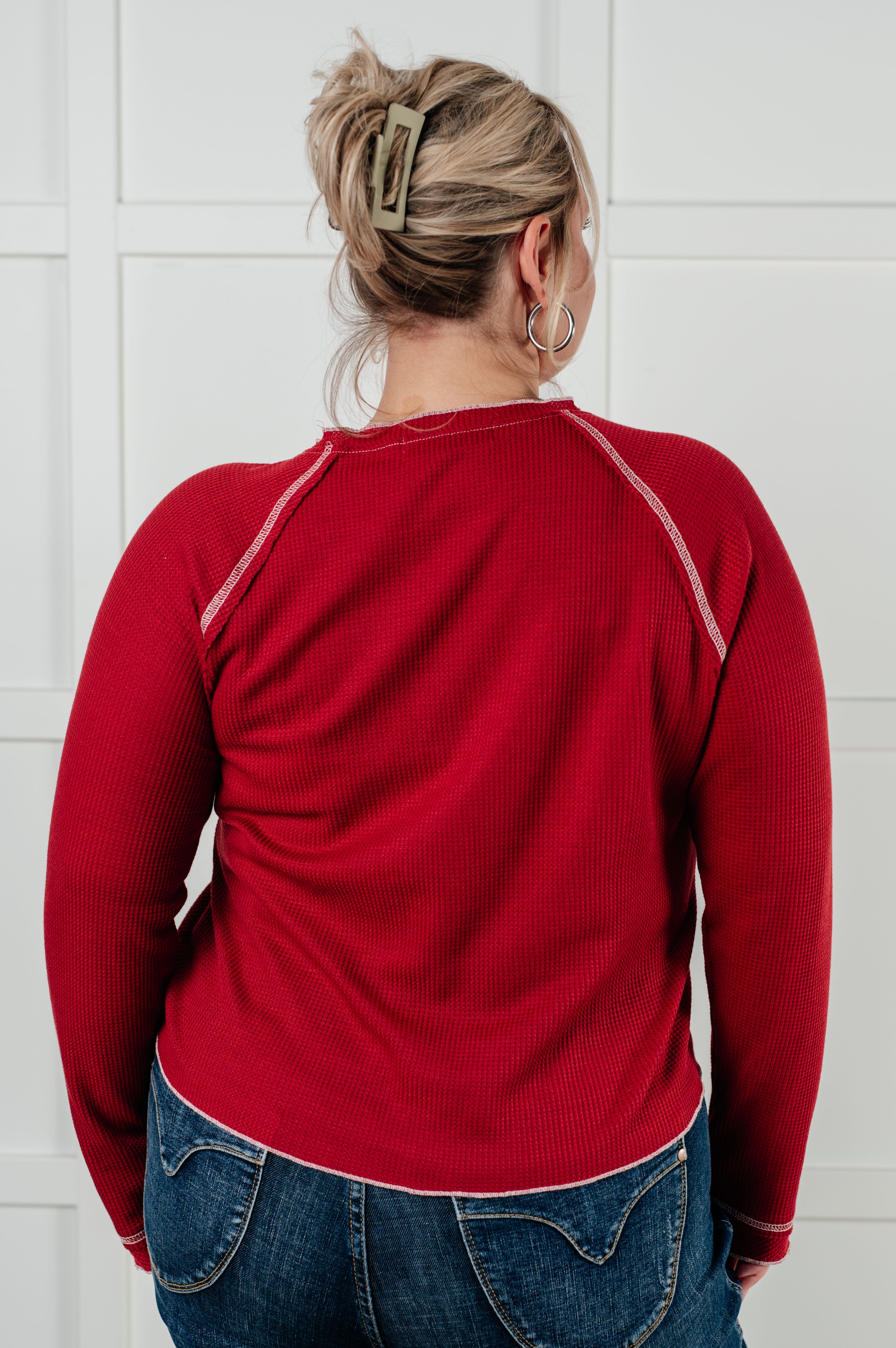 Rear view of person wearing red long sleeve Clever Expression top with contrast stitching and blue jeans indoors