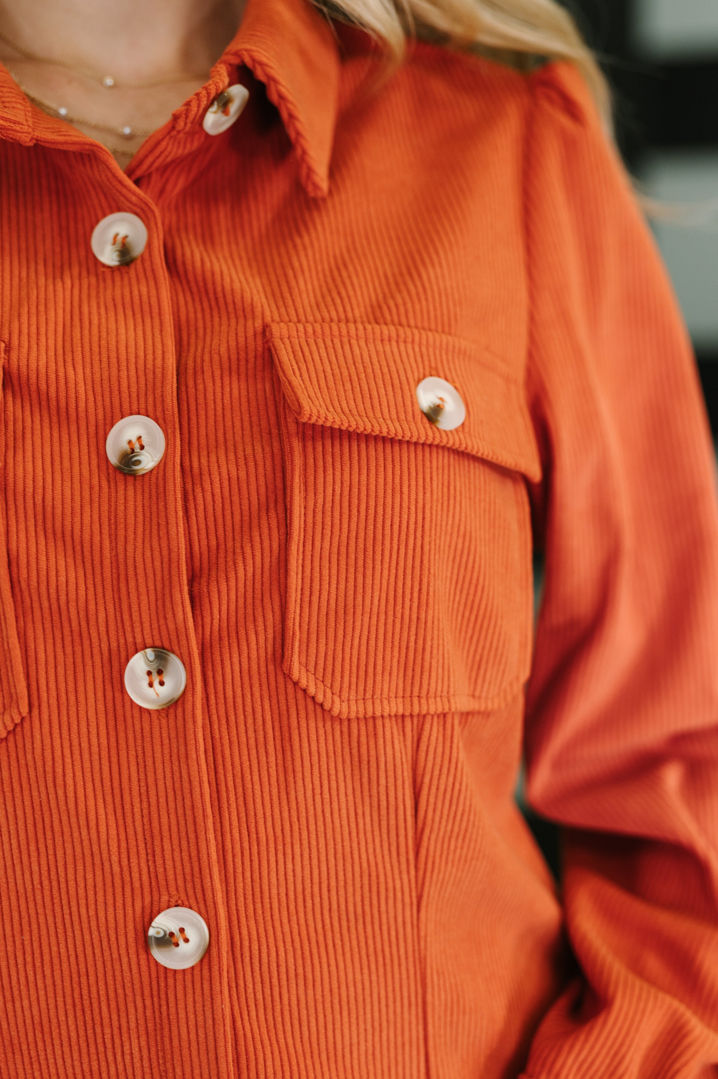 Close-up of burnt orange corduroy shirt dress featuring large white buttons and a front flap pocket