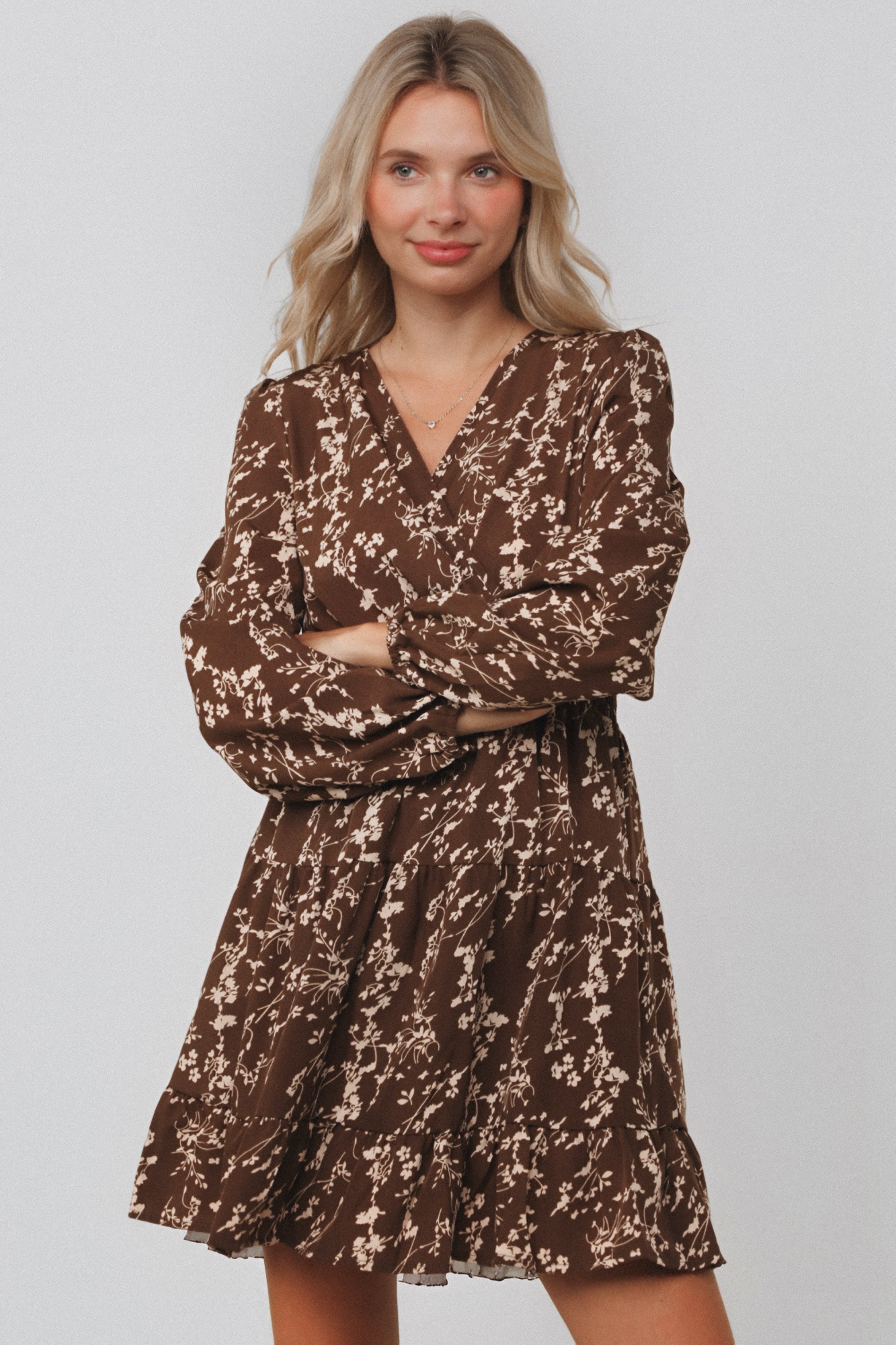 Woman wearing brown floral smocked waist dress with long sleeves and V-neck standing with arms crossed