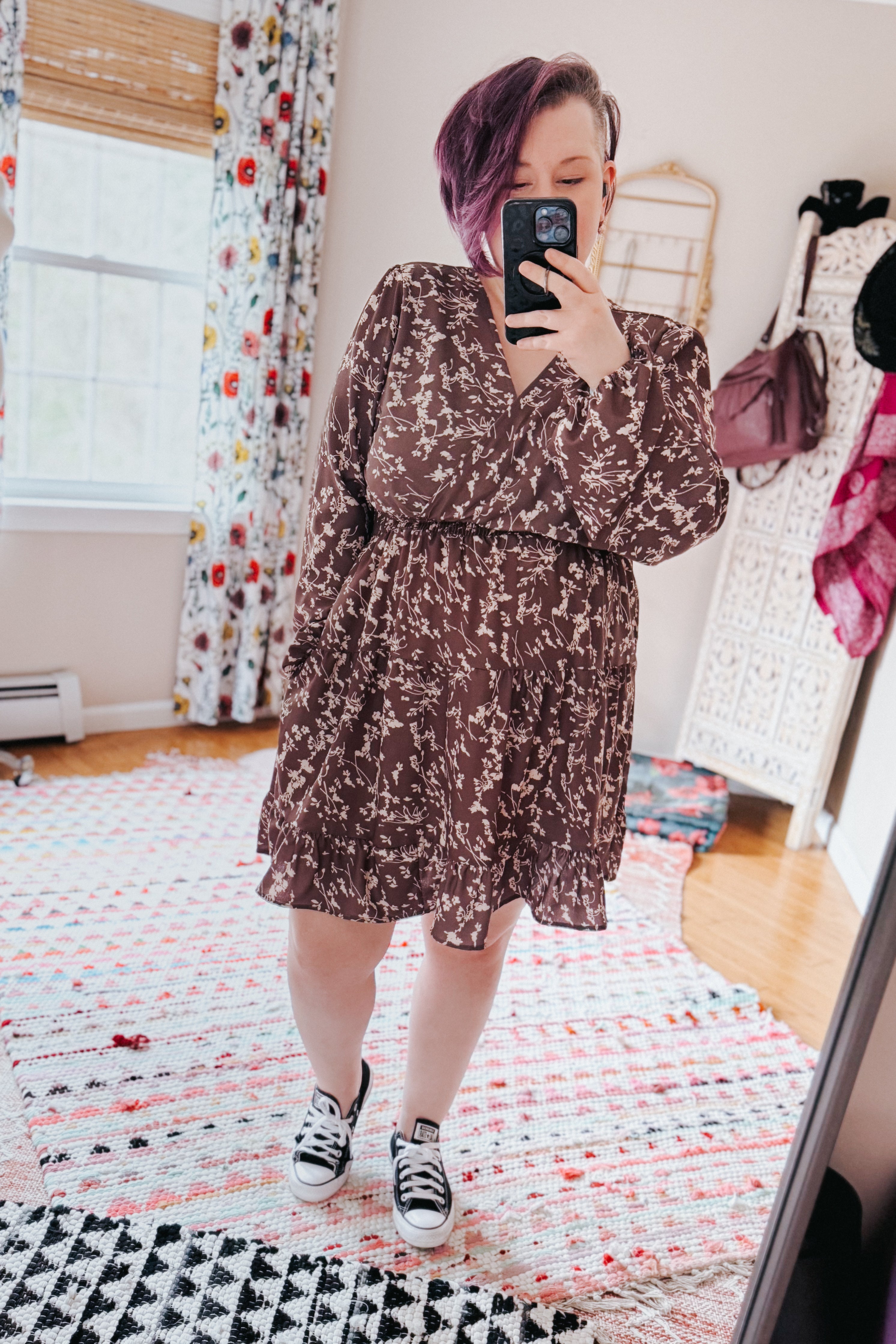 Woman taking mirror selfie wearing brown floral smocked waist dress with long sleeves and V-neck paired with black sneakers