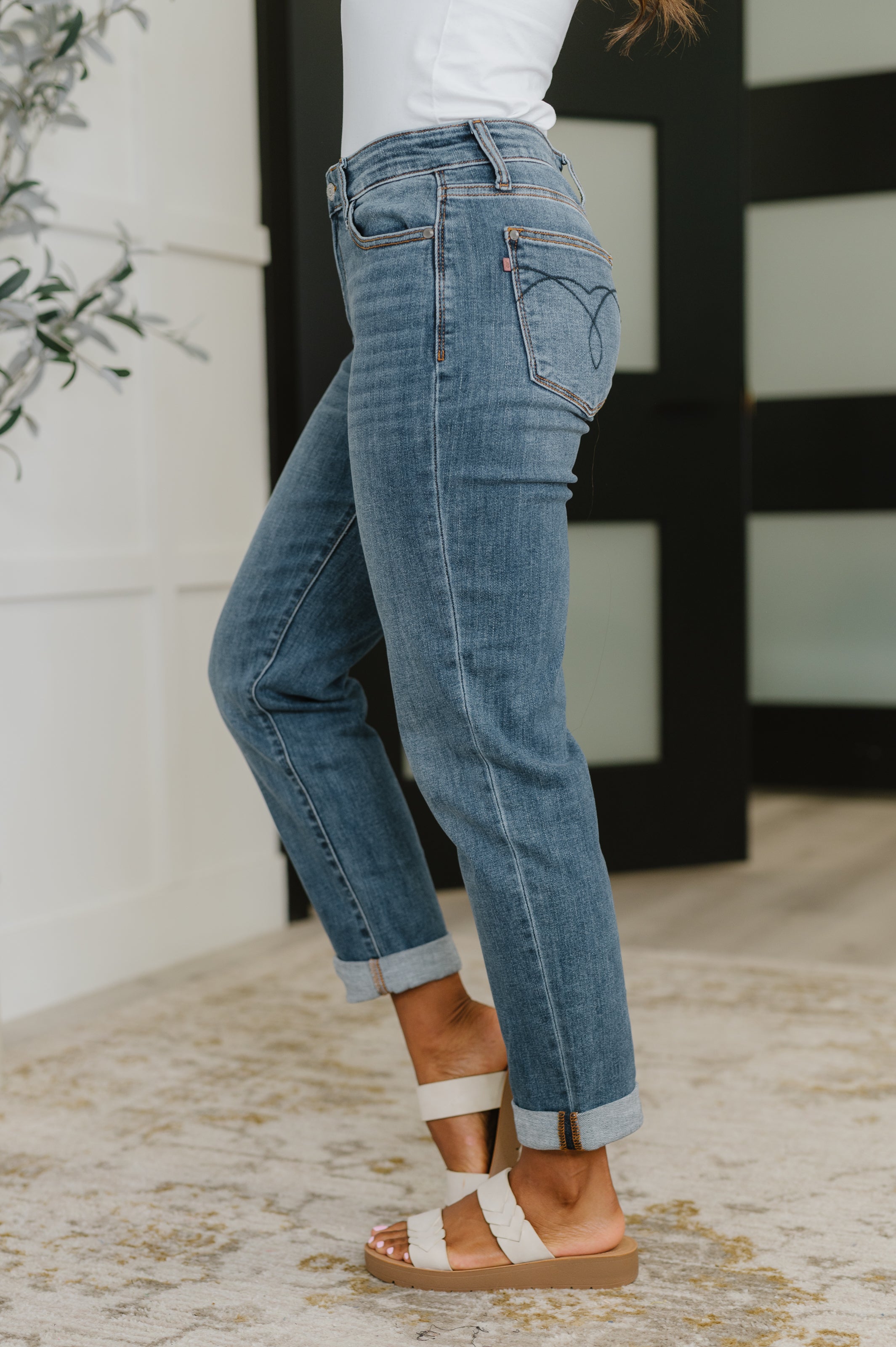 Side view of woman wearing blue boyfriend jeans with cuffed hems and white sandals indoors
