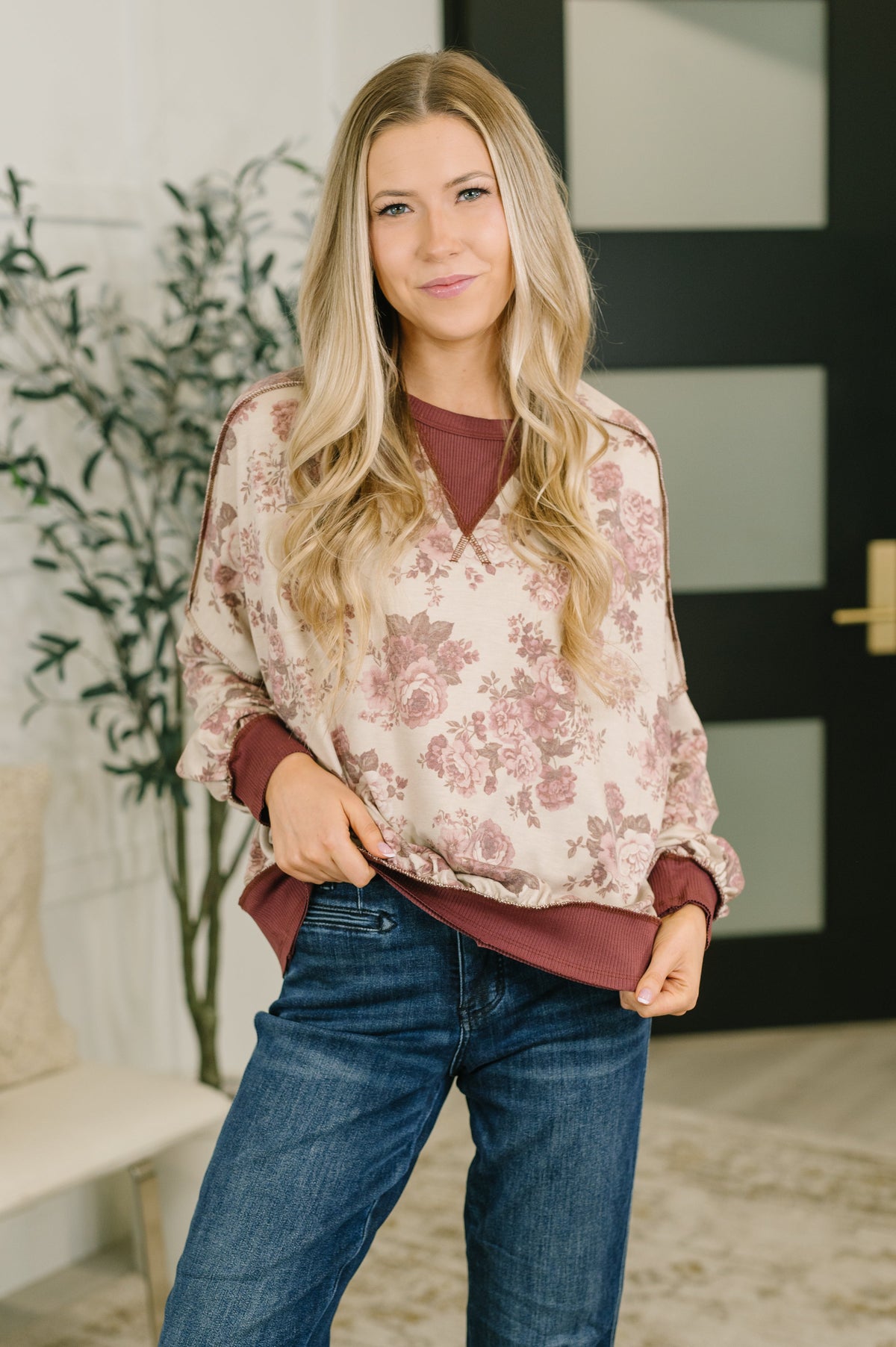 Woman modeling a rust contrast pullover with a floral body and ribbed trim styled with dark blue jeans indoors