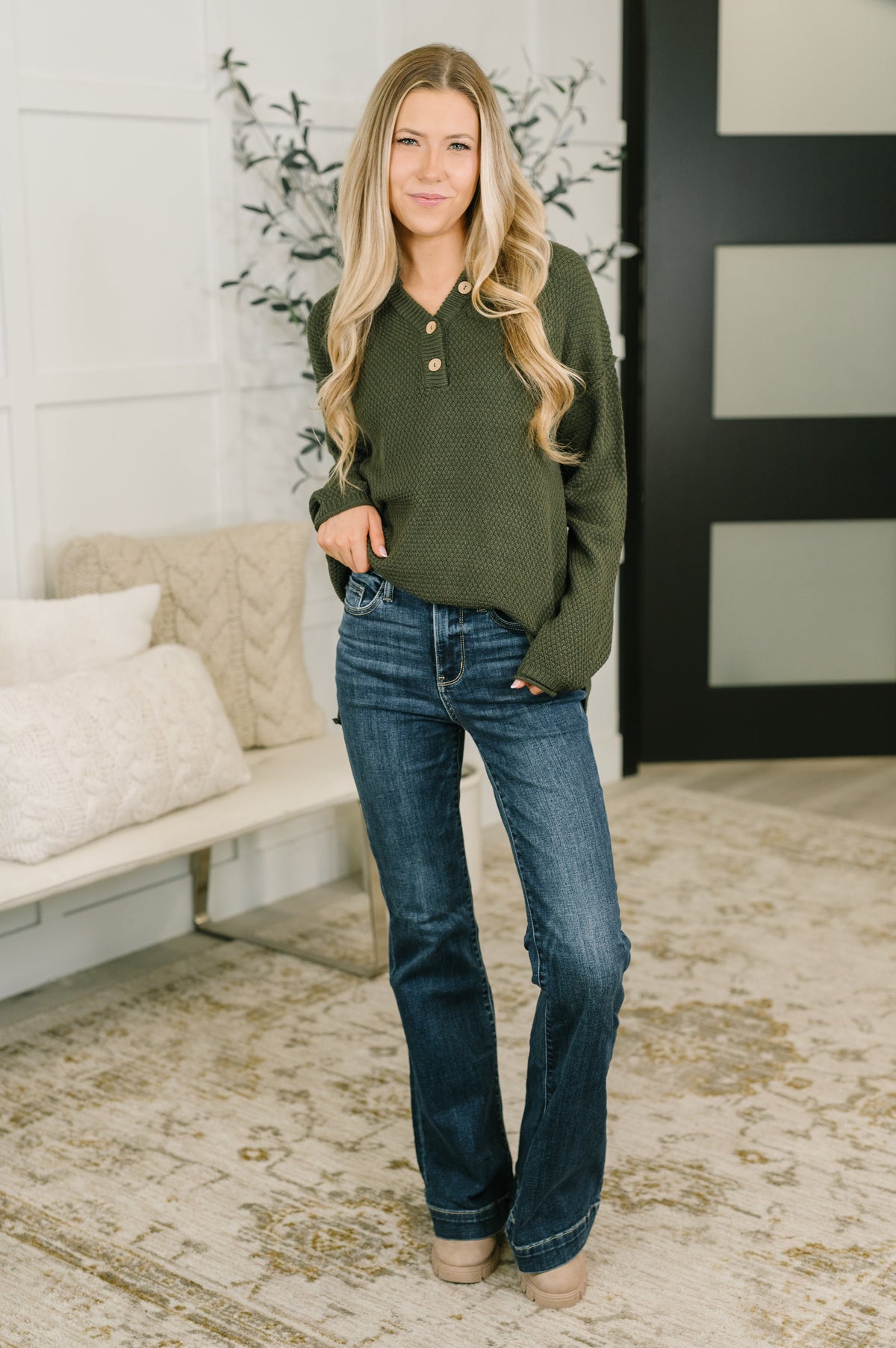 Woman modeling a dark olive sweater knit henley top with a V neck and button placket paired with jeans indoors