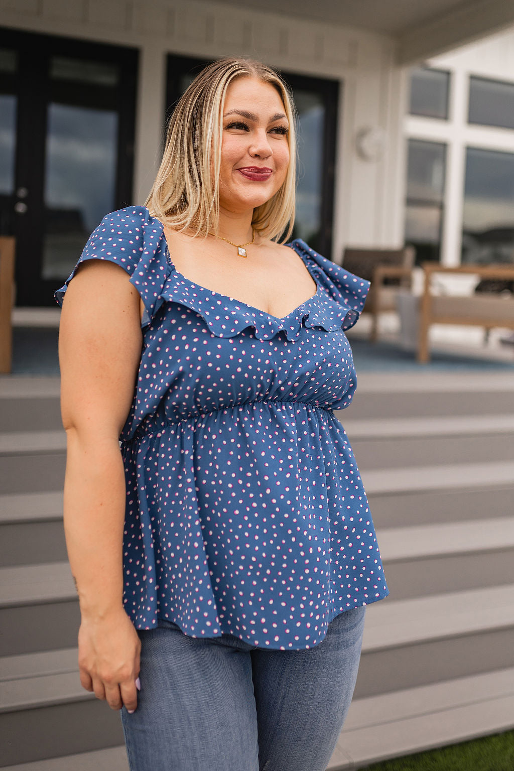 Woman wearing blue peplum blouse with pink polka dots and ruffled neckline standing outdoors on stairs
