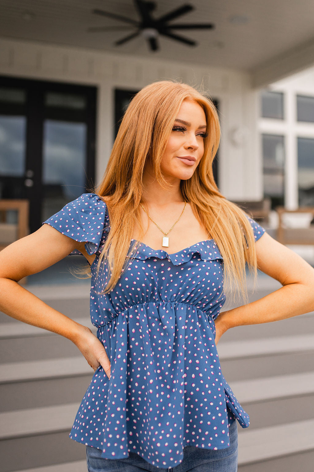 Woman with long blonde hair wearing blue Connect the Dots peplum blouse with flutter sleeves standing outdoors near steps
