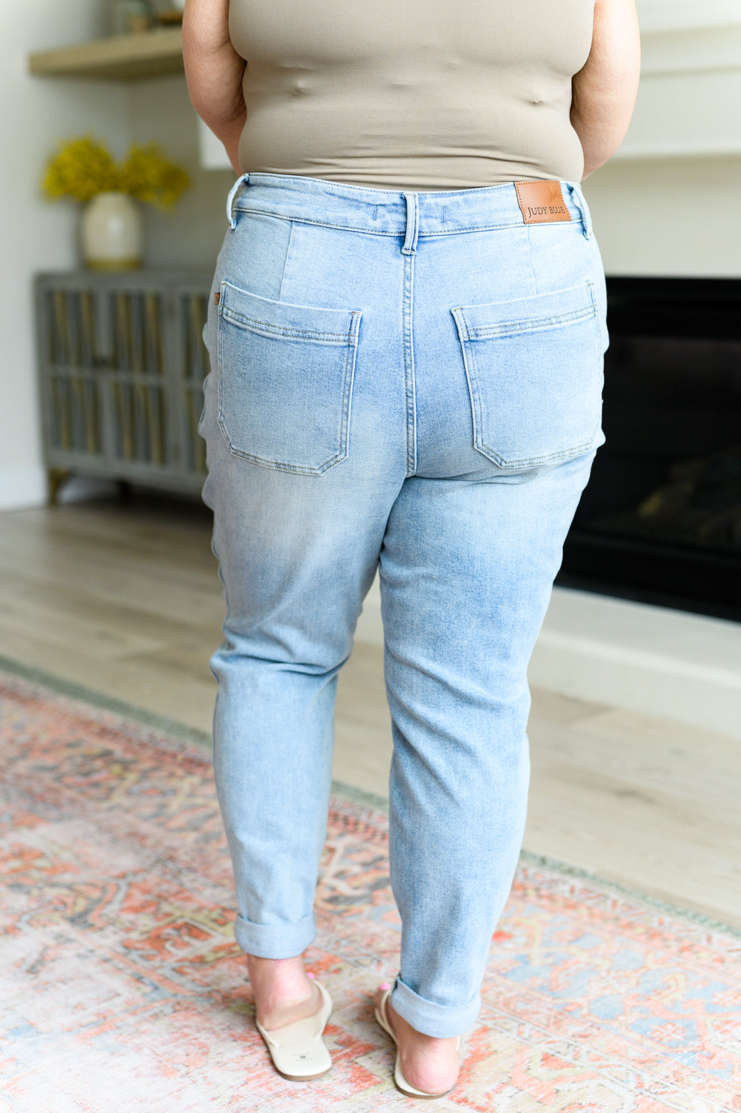 Plus size model wearing light wash high rise denim joggers with back pockets standing indoors on patterned rug