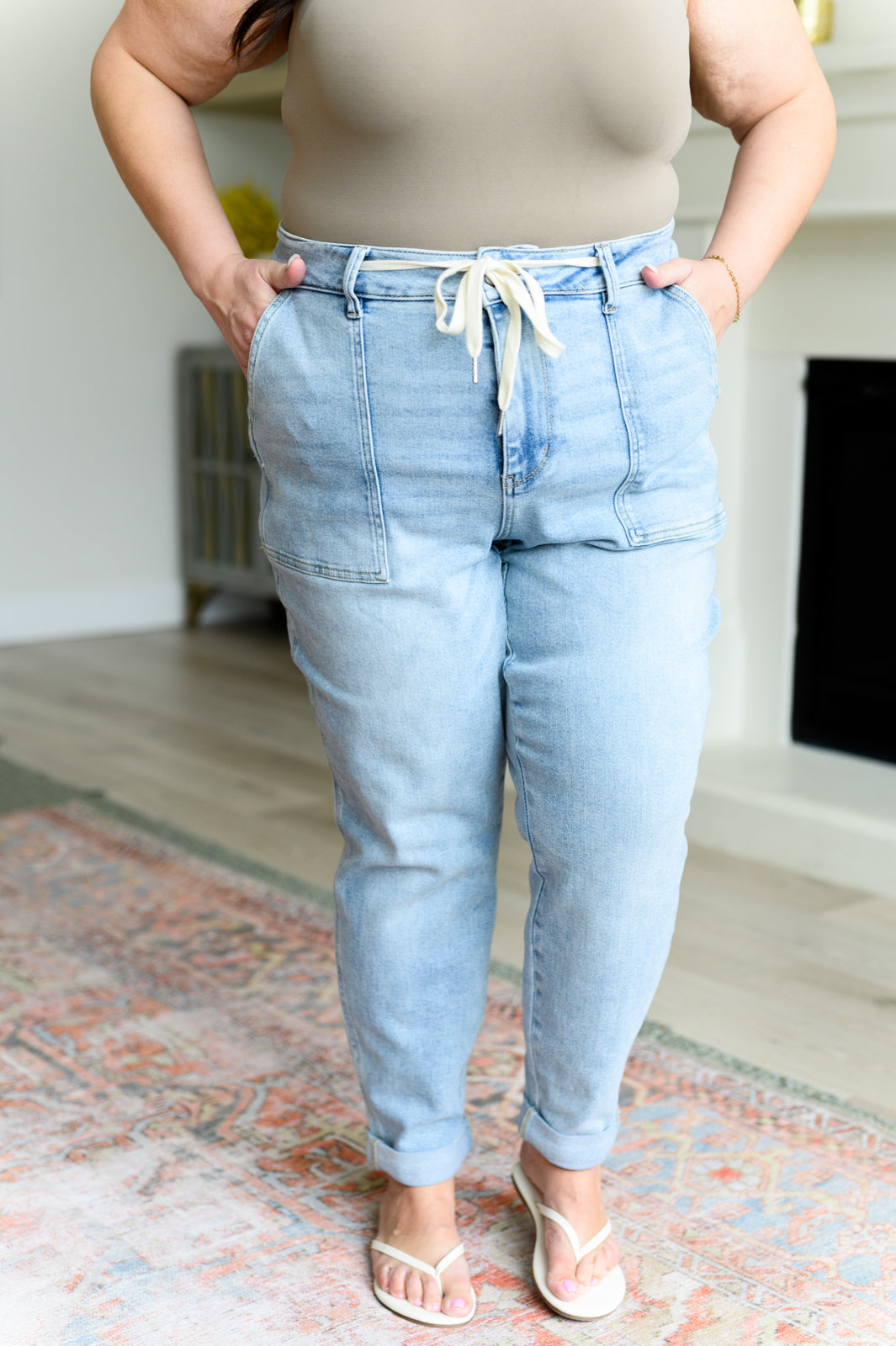 Plus size model wearing light wash high rise vintage denim joggers with front patch pockets and drawstring waist indoors