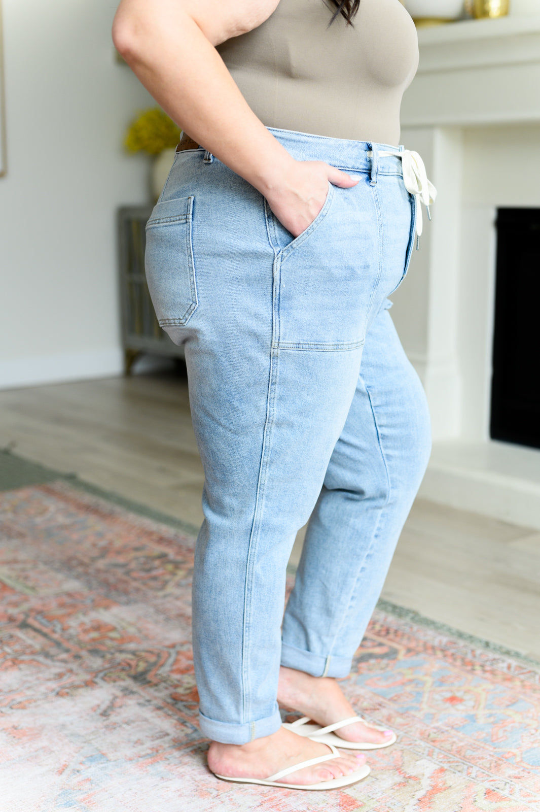 Plus size woman wearing light wash high rise vintage denim jogger pants and beige tank top indoors by fireplace