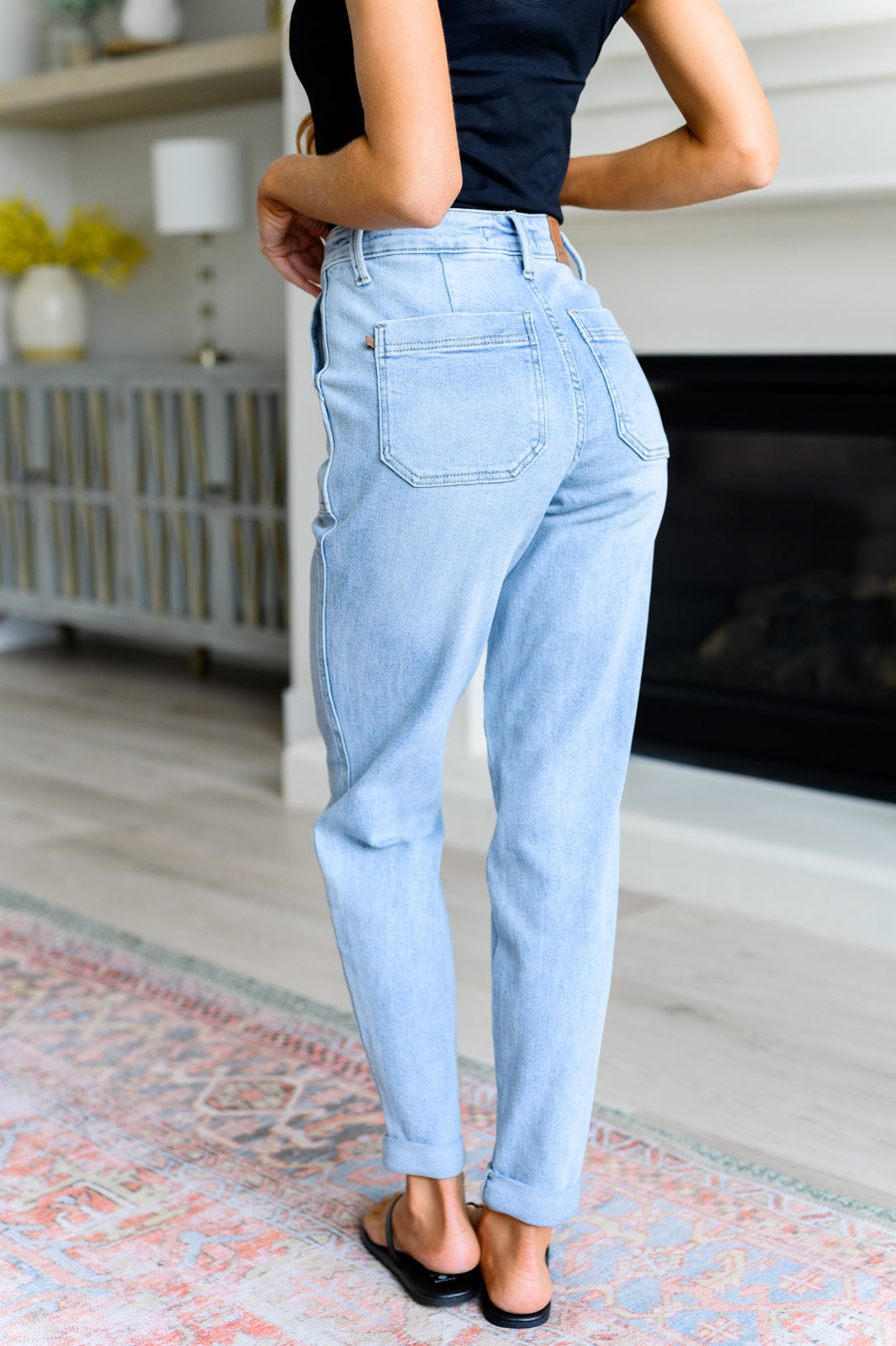 Woman wearing light wash high rise vintage denim joggers standing indoors near fireplace on patterned rug