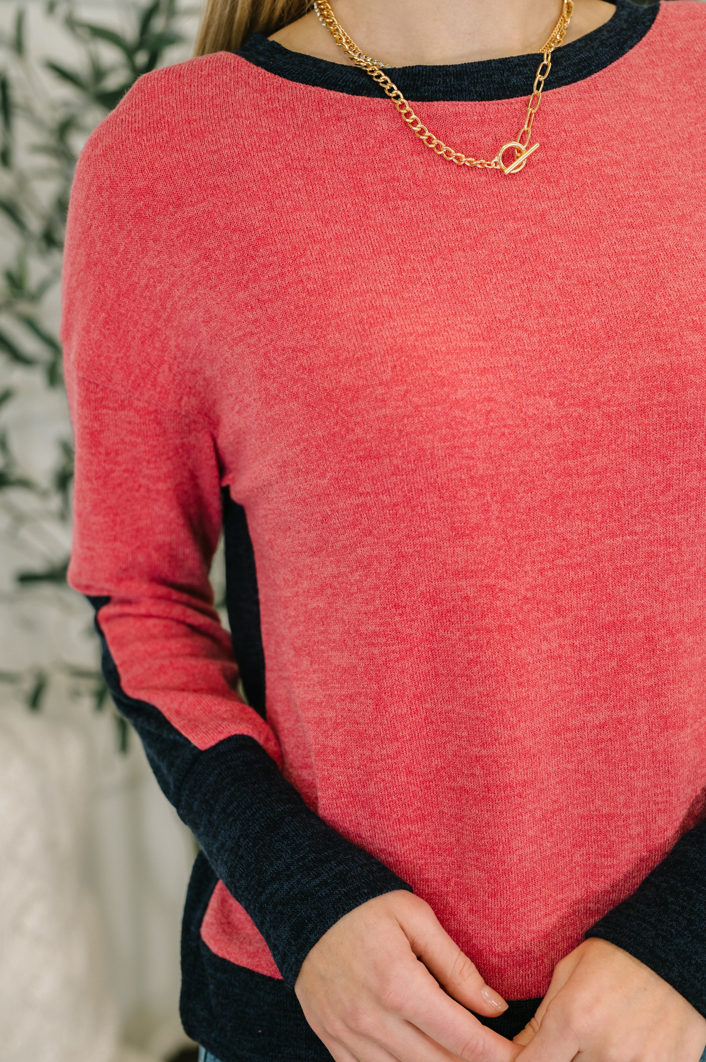 Woman wearing a red sweater with black sleeves and a gold necklace.