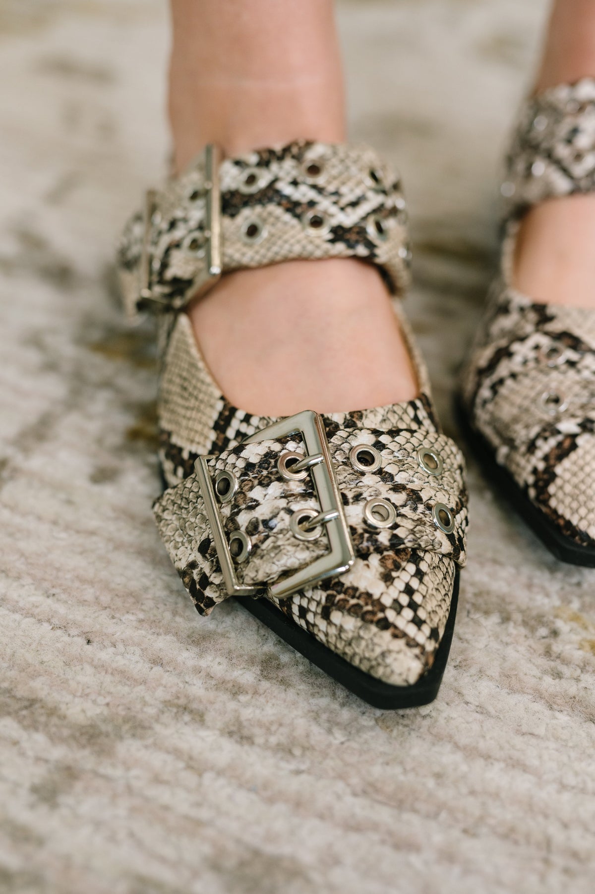 Grey snakeskin pointy toe flats with oversized bronze buckles and slingback straps styled on a textured rug