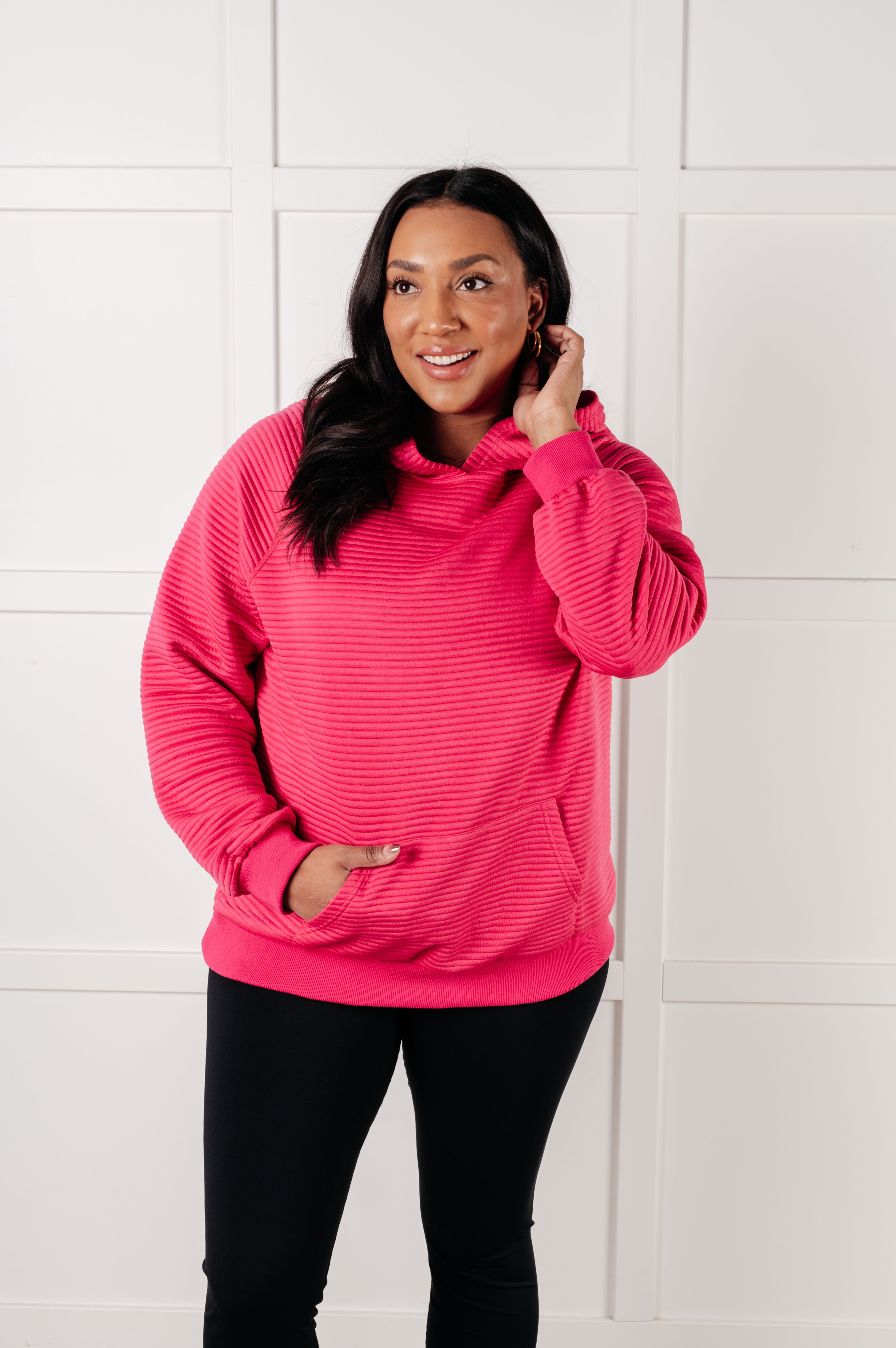 Smiling plus size woman wearing bright rose textured hoodie with hand in front pocket standing indoors