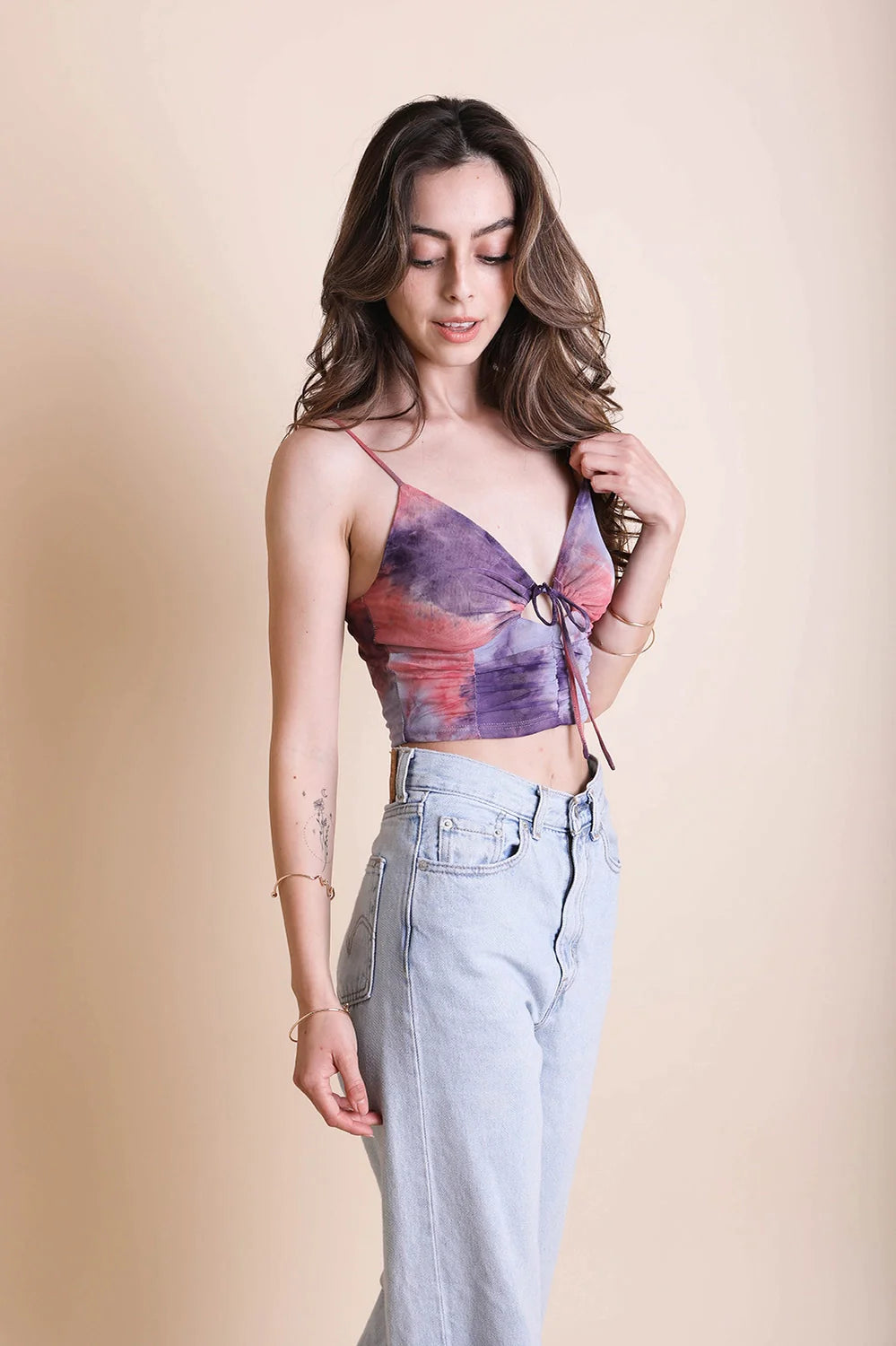 Woman wearing purple and pink tie dye brami top with front ring detail paired with light wash high-waisted jeans