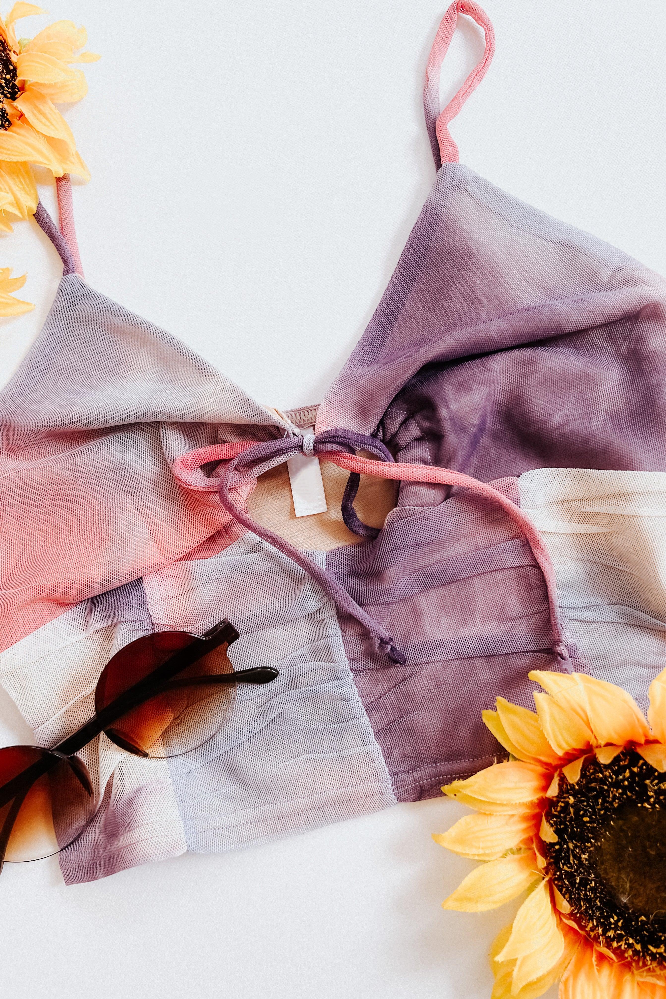 Tie dye mesh brami top in shades of pink and purple with sunglasses and sunflowers on white surface