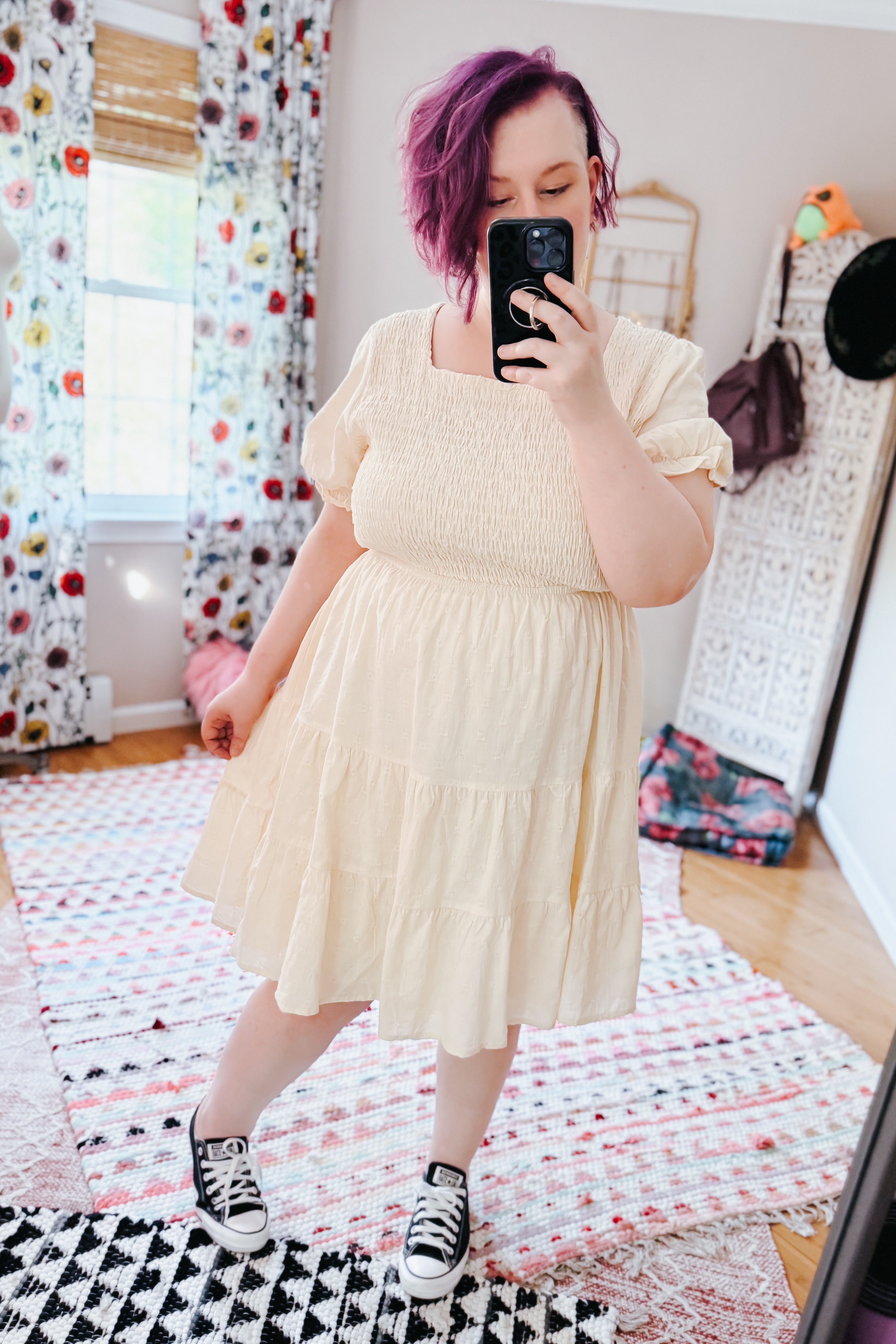 Woman with purple hair wearing an ivory square neck dress with puff sleeves and sneakers in an eclectic room