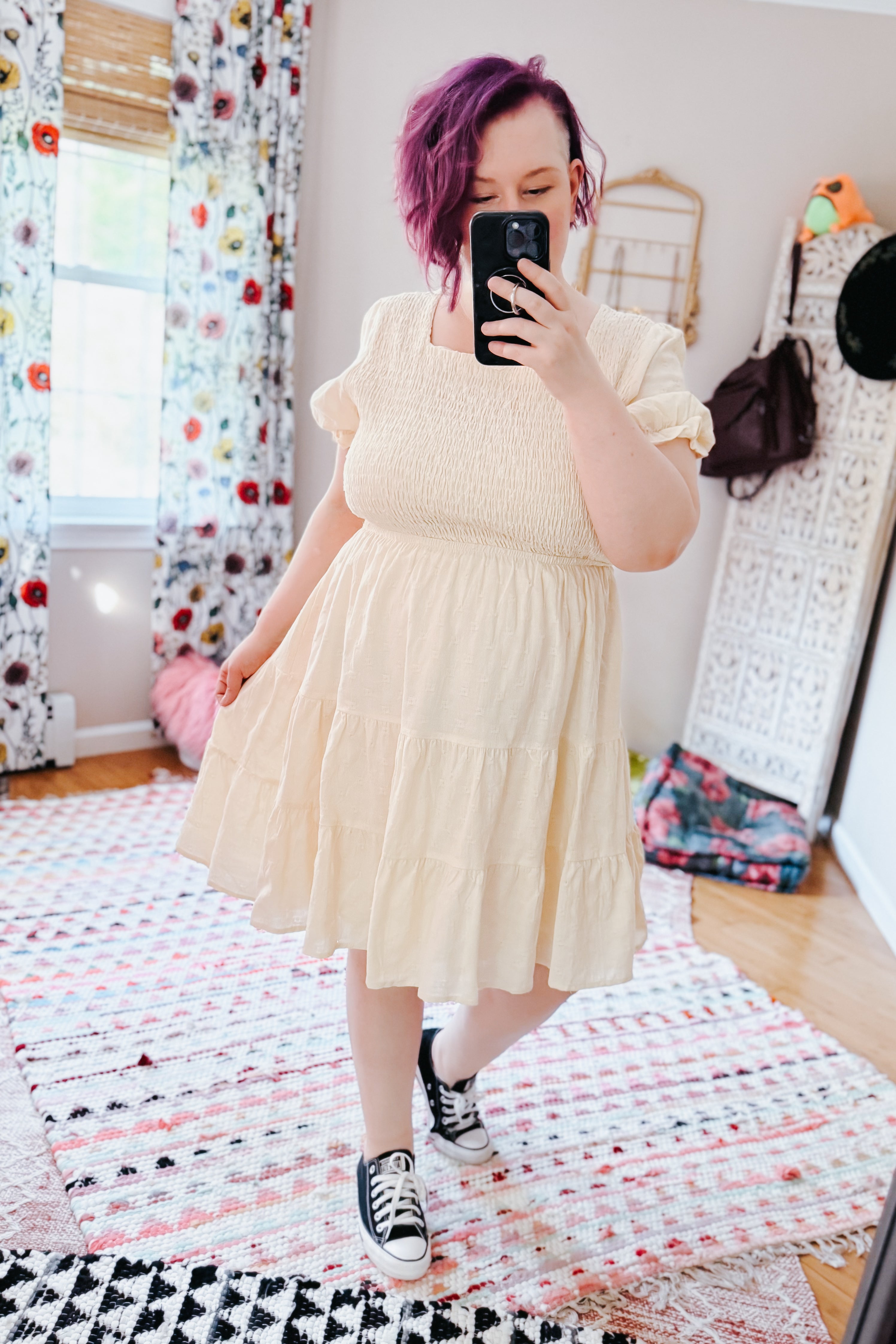 Woman with purple hair wearing an ivory square neck dress with tiered skirt and sneakers in a size inclusive eclectic room