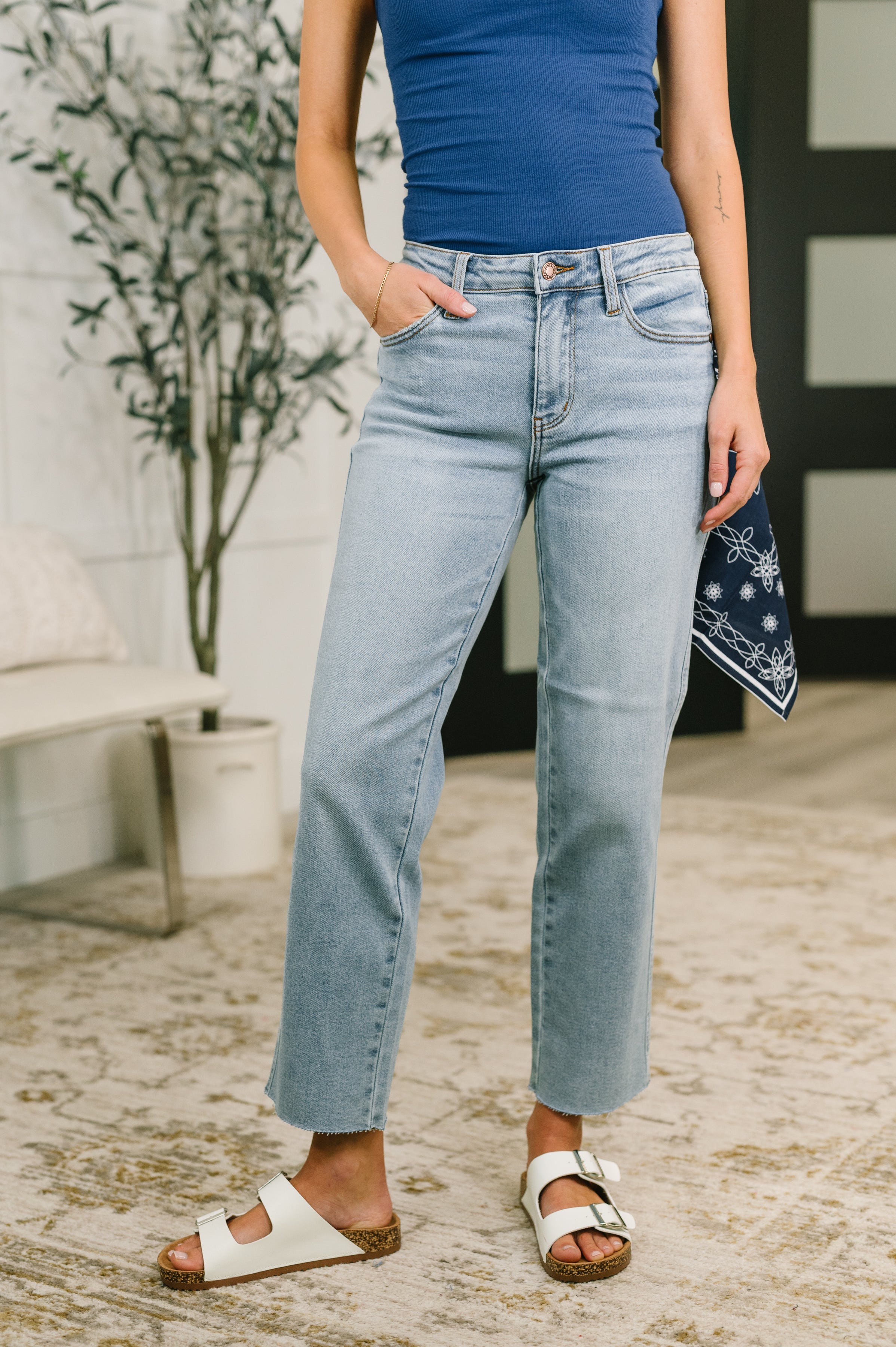 Woman wearing blue mid rise straight leg jeans with cropped hem and bandana loop paired with white sandals indoors