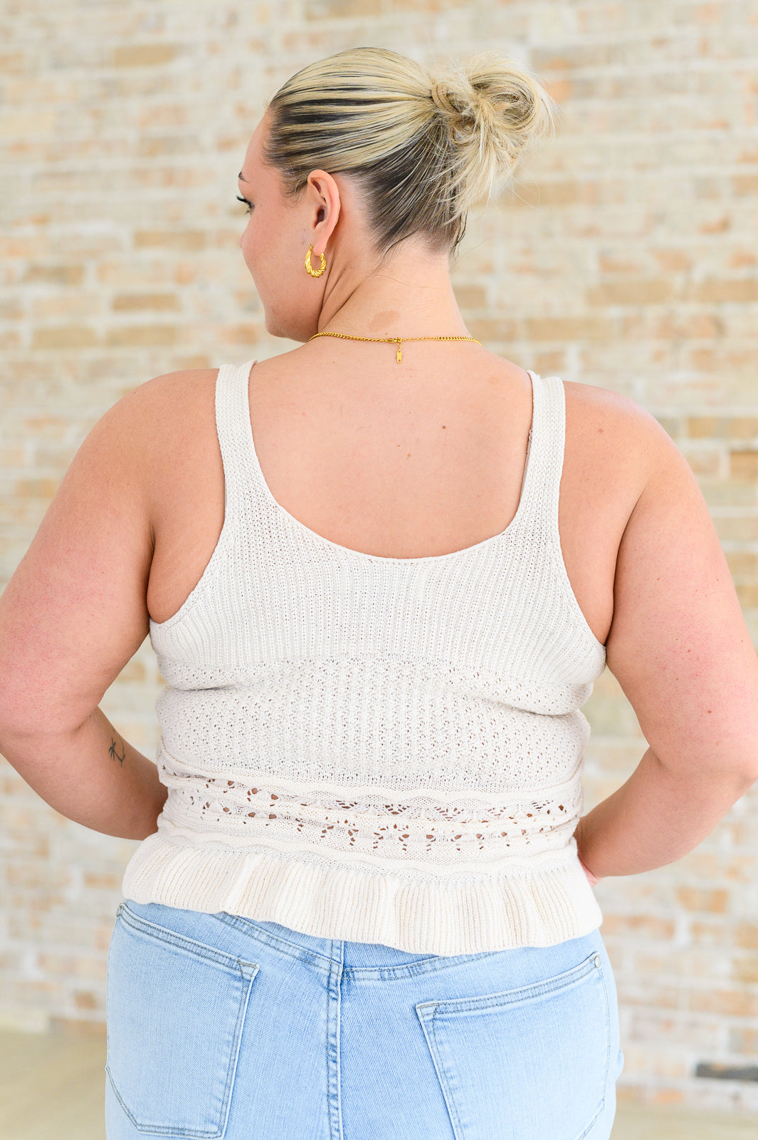Back view of woman wearing cream Day Dancing Ruffle Knit Tank Top with textured knit and ruffle hem indoors