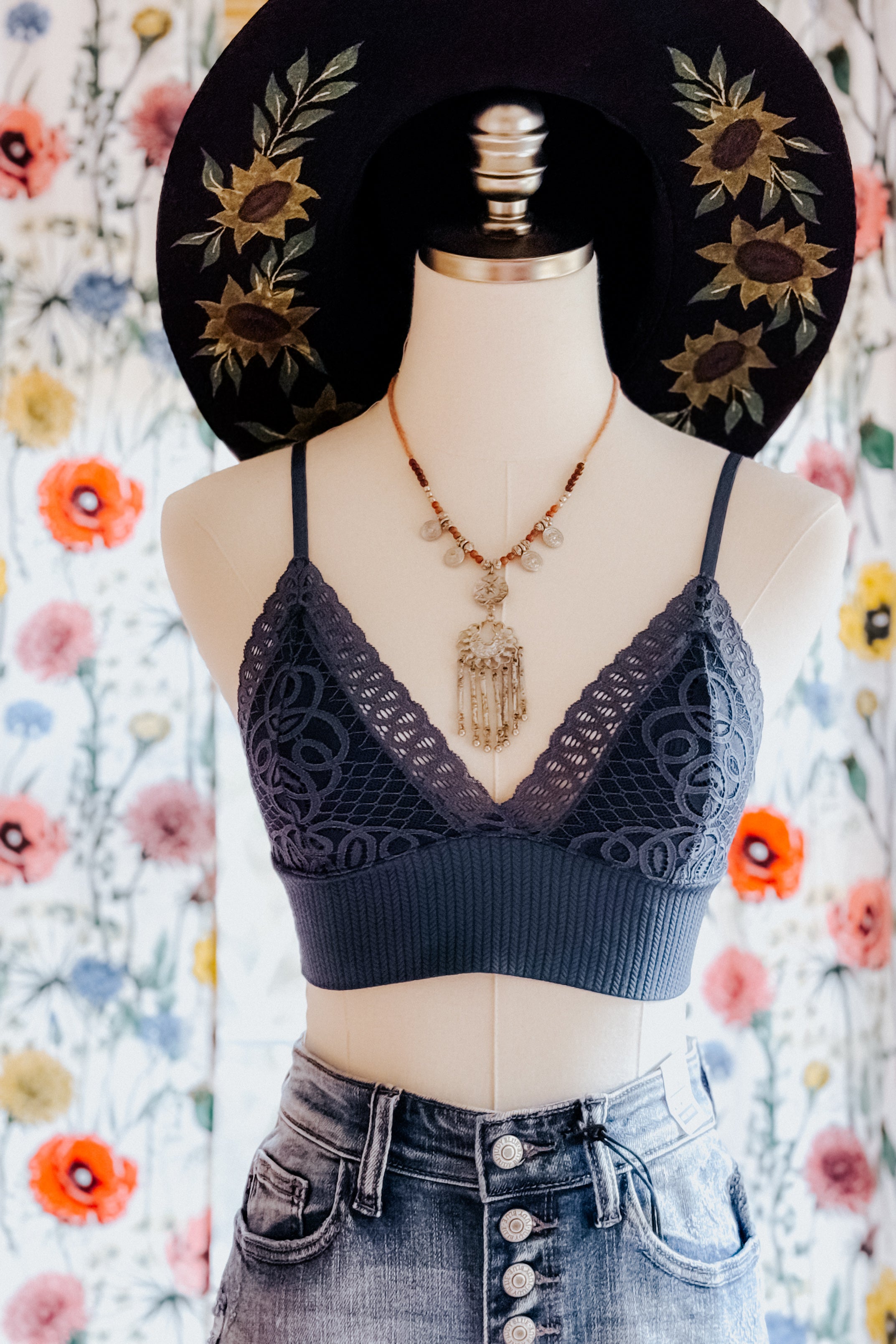Dusty blue lace bralette with intricate geometric pattern styled on mannequin with denim skirt and decorative necklace