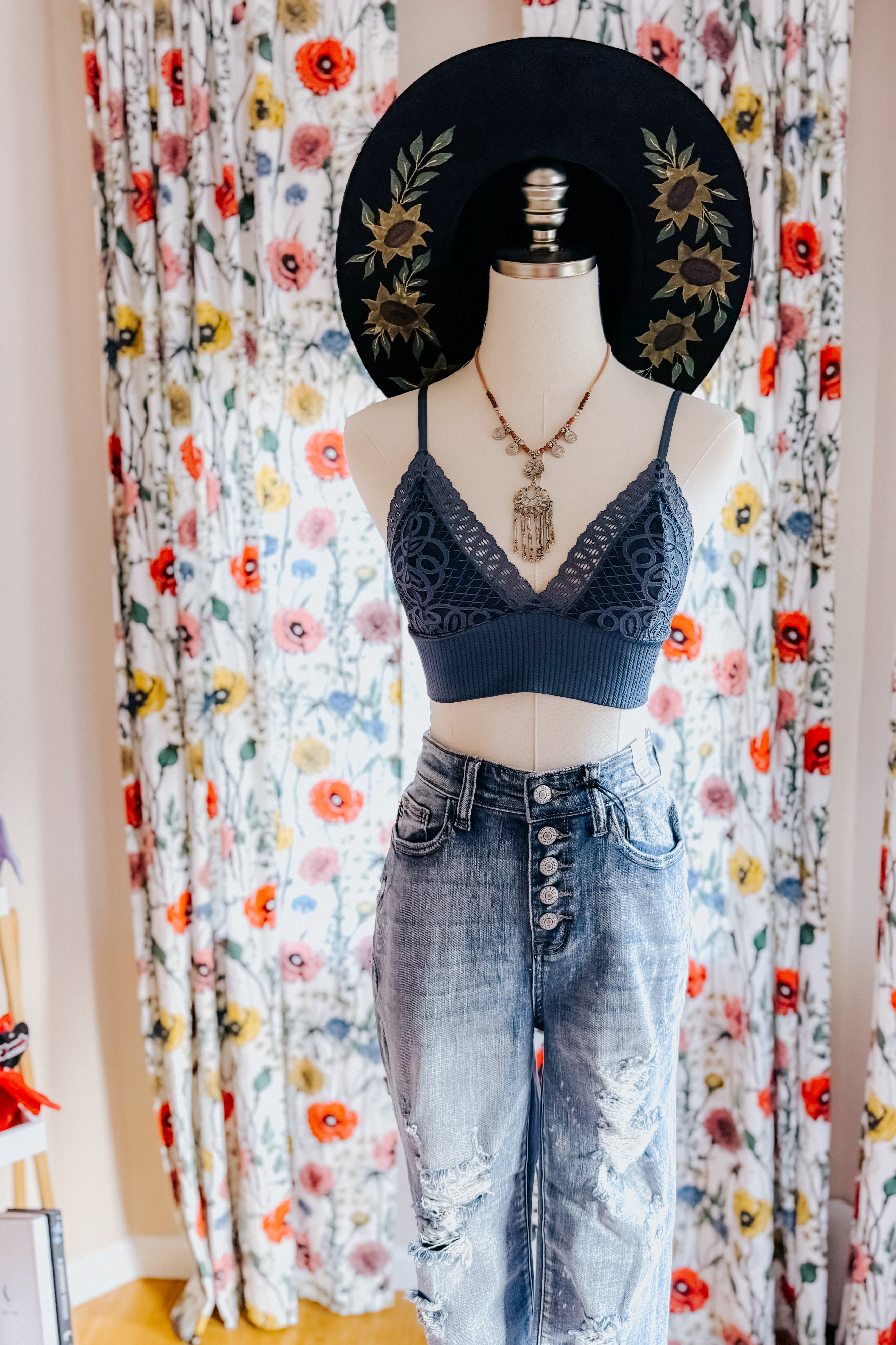 Dusty blue lace bralette with scalloped edges styled on mannequin with distressed high-waisted jeans and black floral hat