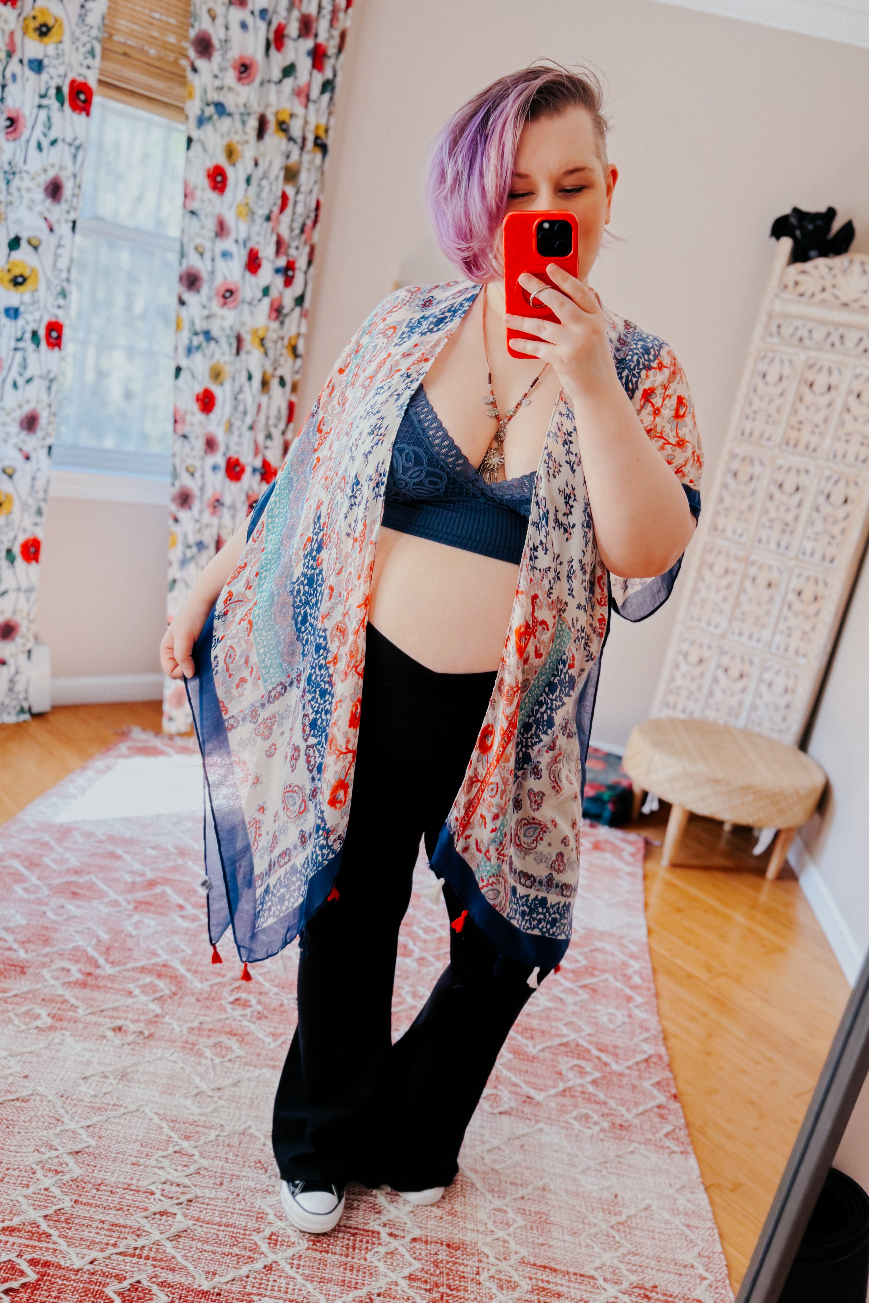 Person with short purple hair wearing dusty blue lace bralette and patterned sheer kimono, taking mirror selfie in cozy room