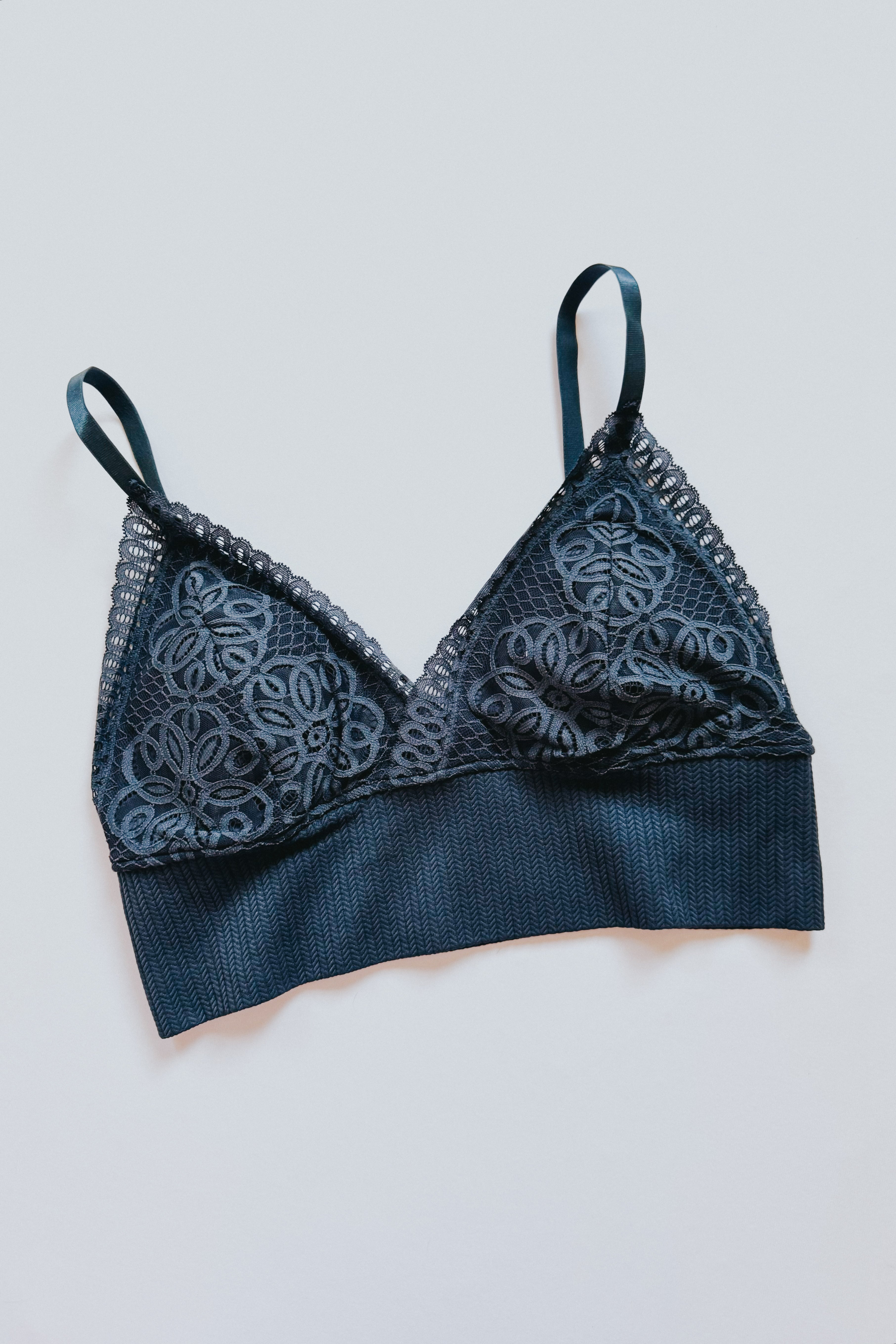 Lace bralette in deep dusty blue with floral mesh cups and wide textured band on light gray surface