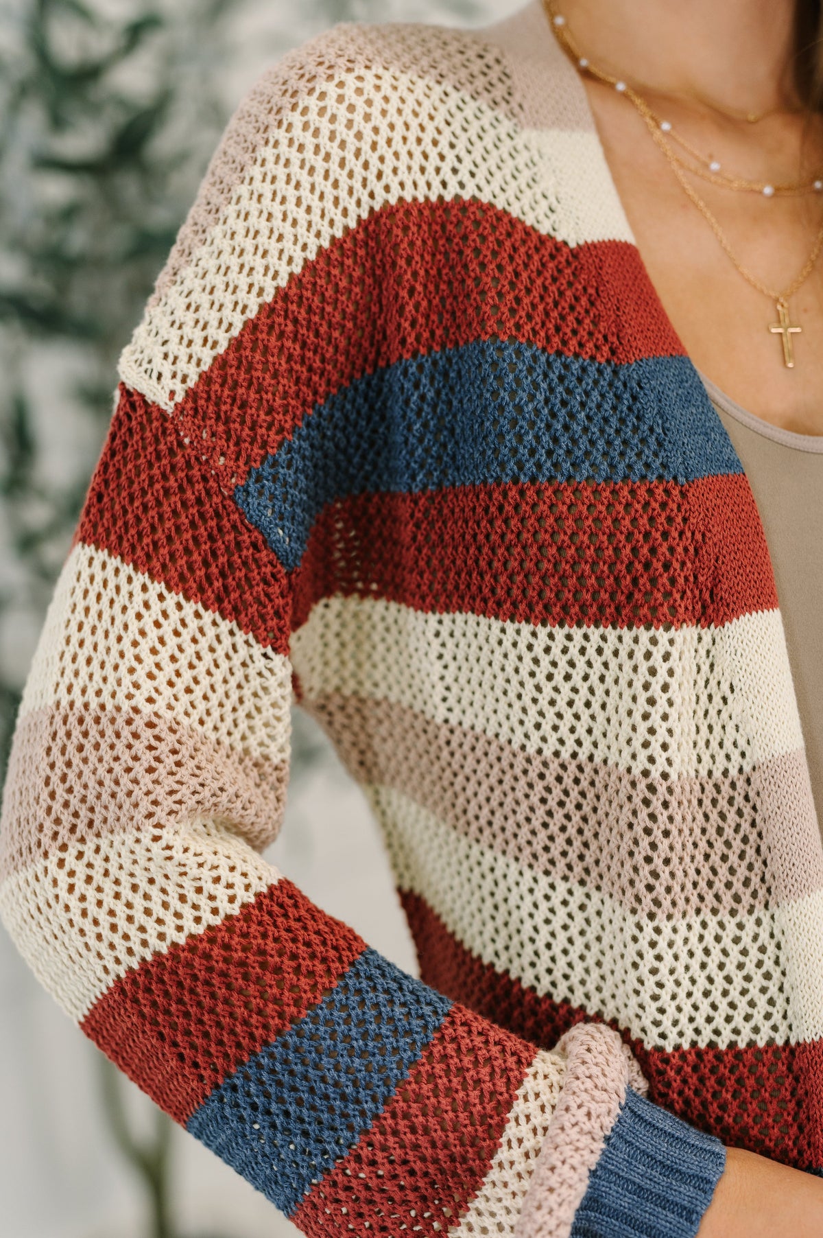 Close view of a woman in a rust striped open front knit cardigan over a taupe top with layered gold necklaces