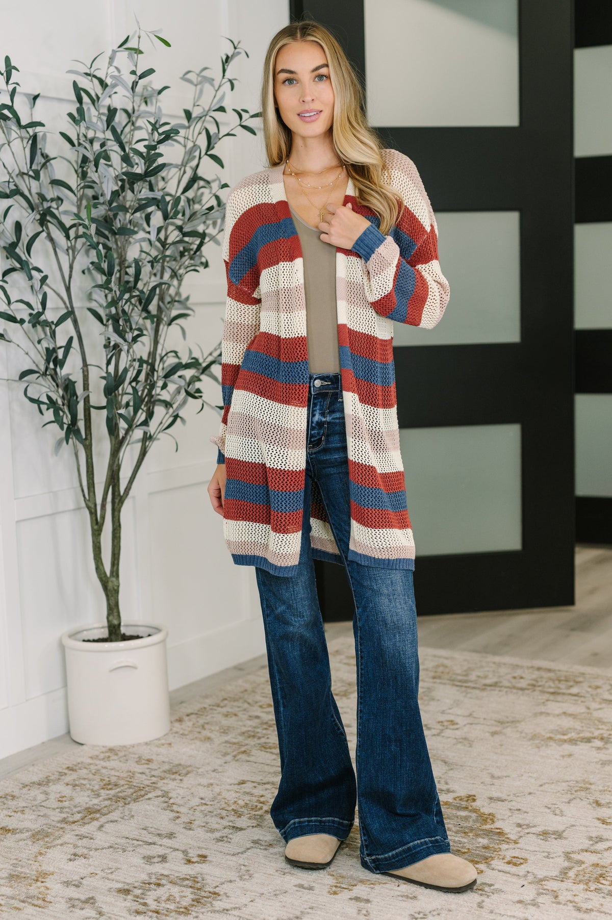 Woman wearing a Rust striped open front knit cardigan over a neutral top with flared jeans in a bright modern home interior