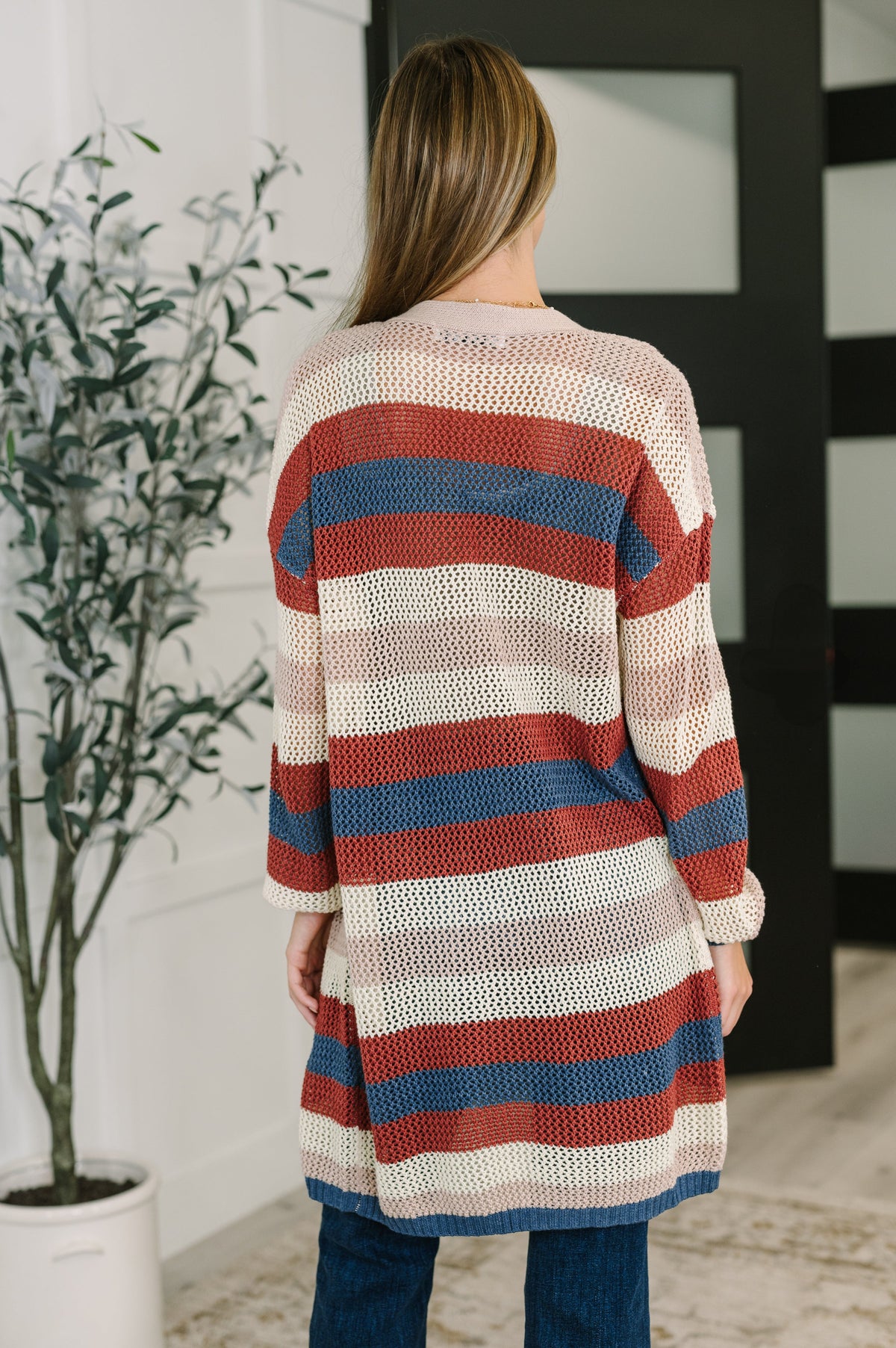 Woman seen from behind wearing a rust striped knit cardigan with ribbed trim and blue jeans in a modern interior