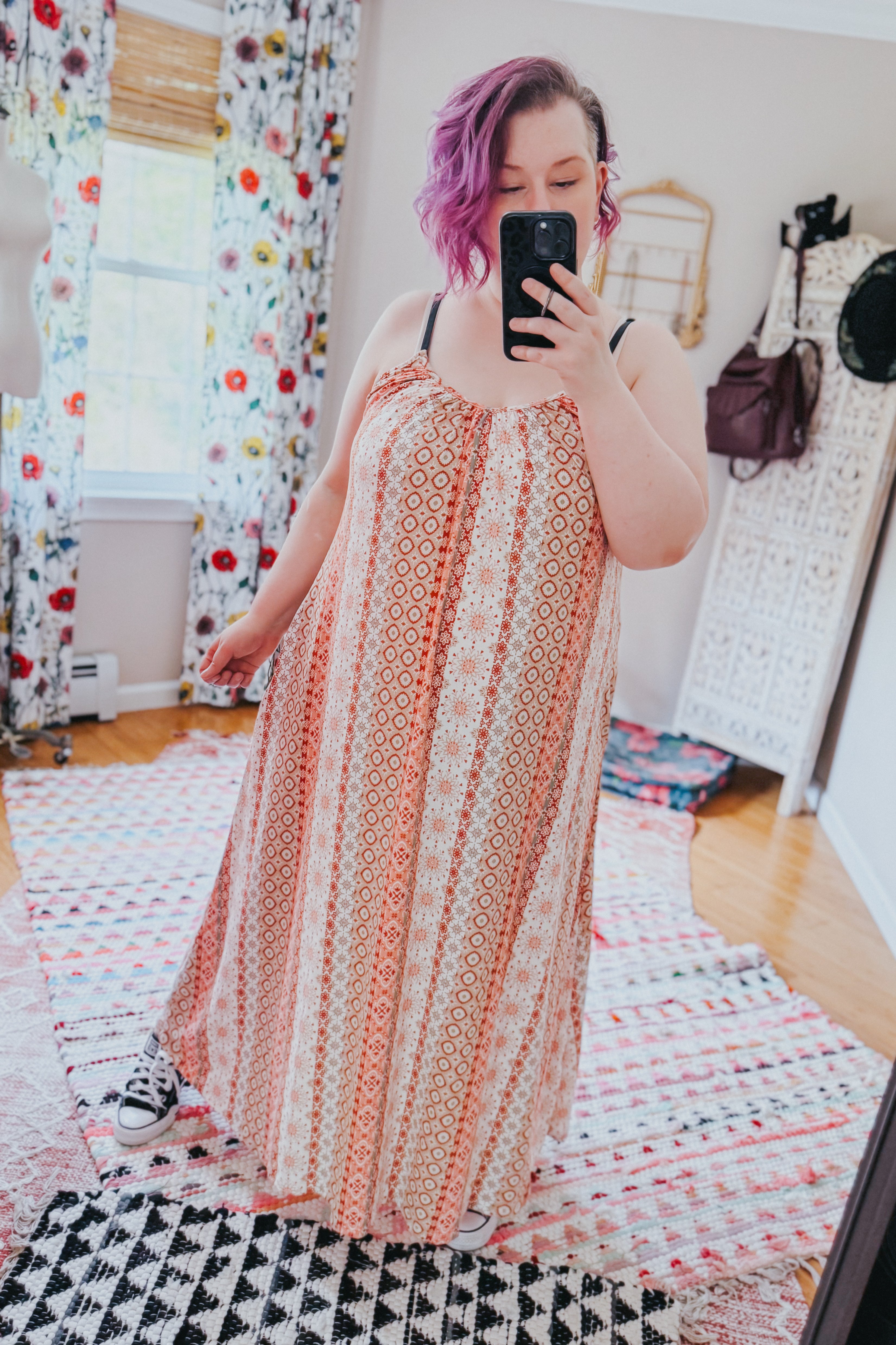 Woman with short purple hair taking mirror selfie wearing patterned flowy maxi dress with sneakers indoors