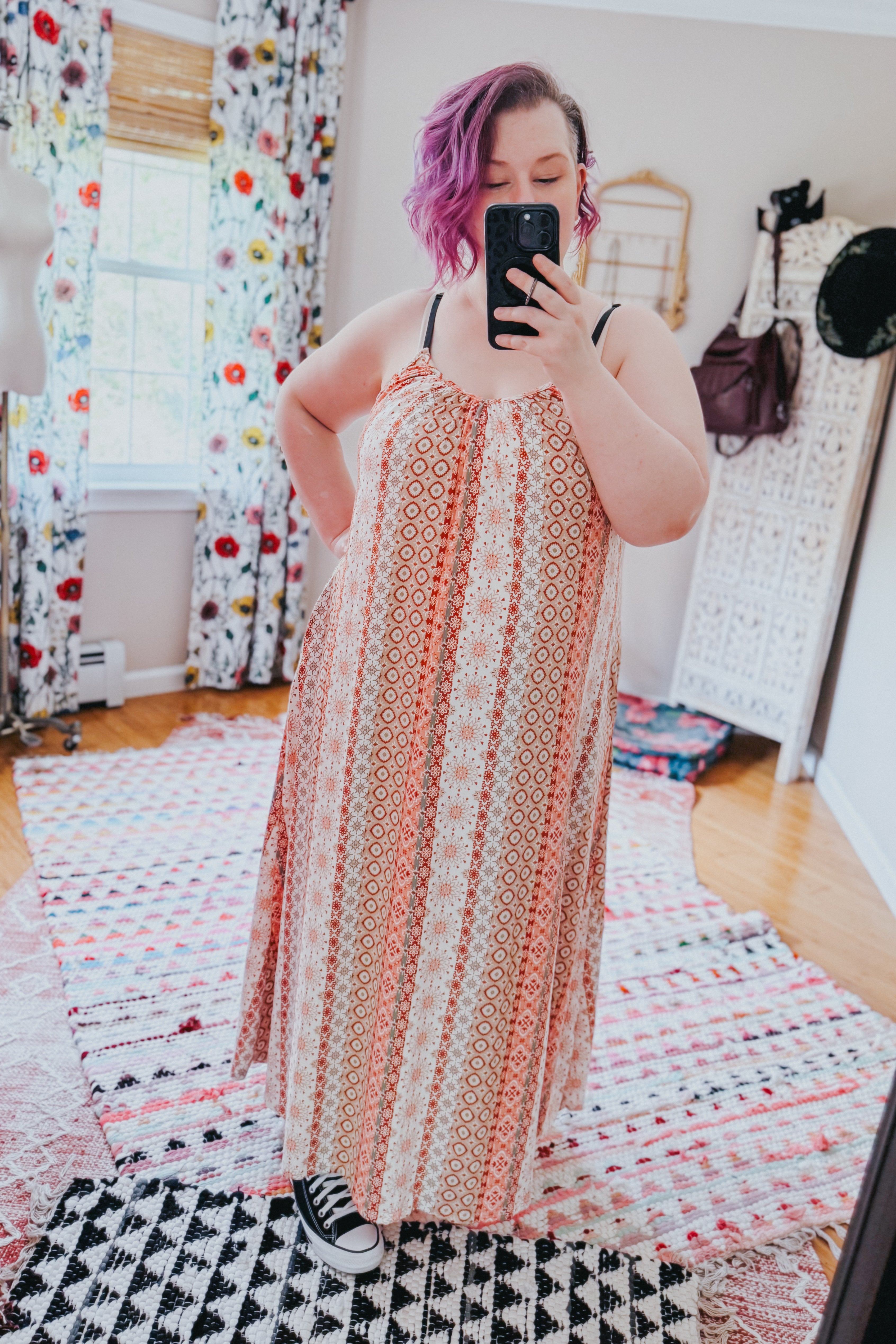 Woman with short purple hair wearing patterned sleeveless maxi dress with sneakers taking a selfie indoors
