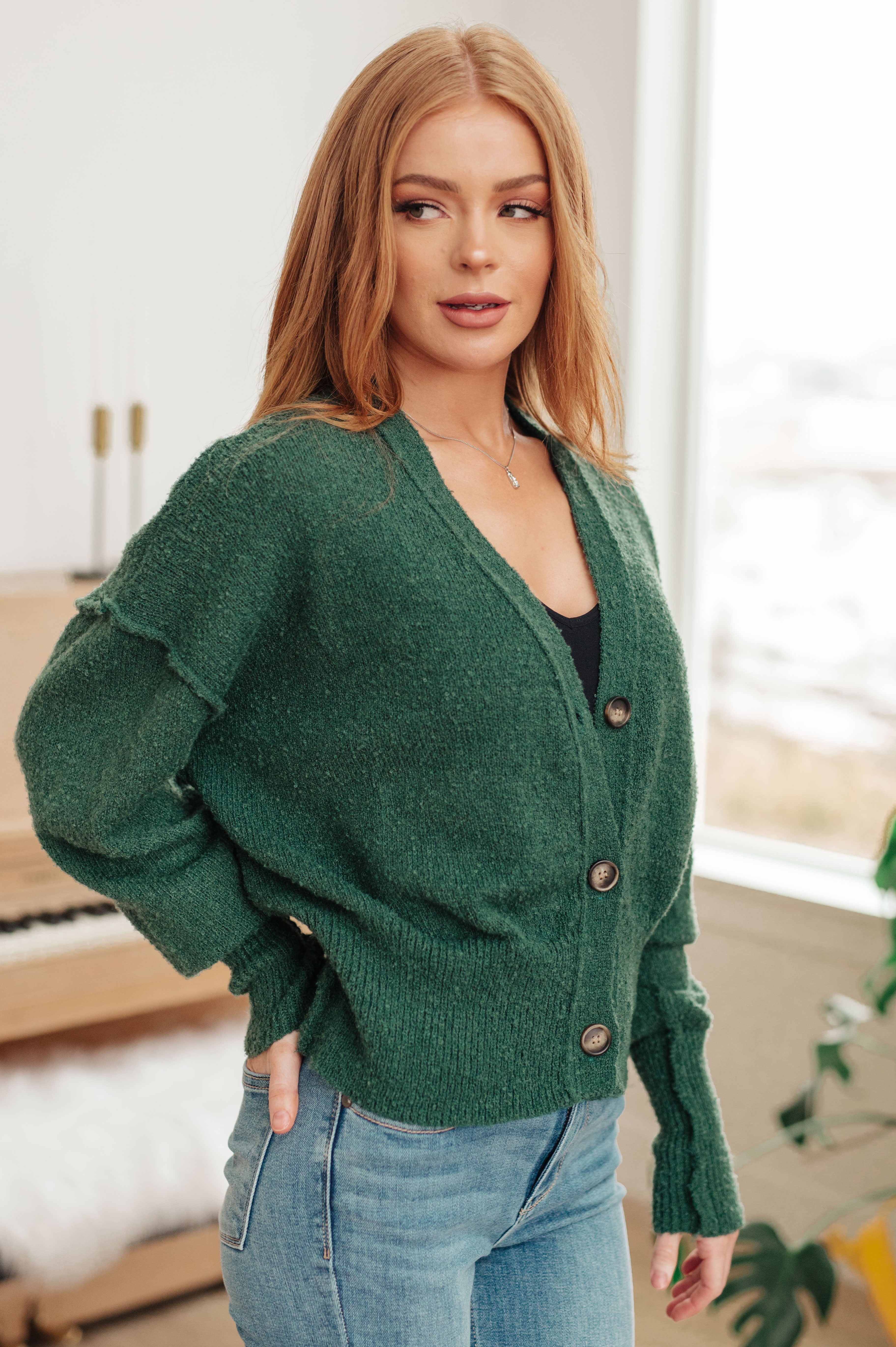 Woman wearing deep green button-up cardigan with relaxed fit and light wash jeans indoors near piano