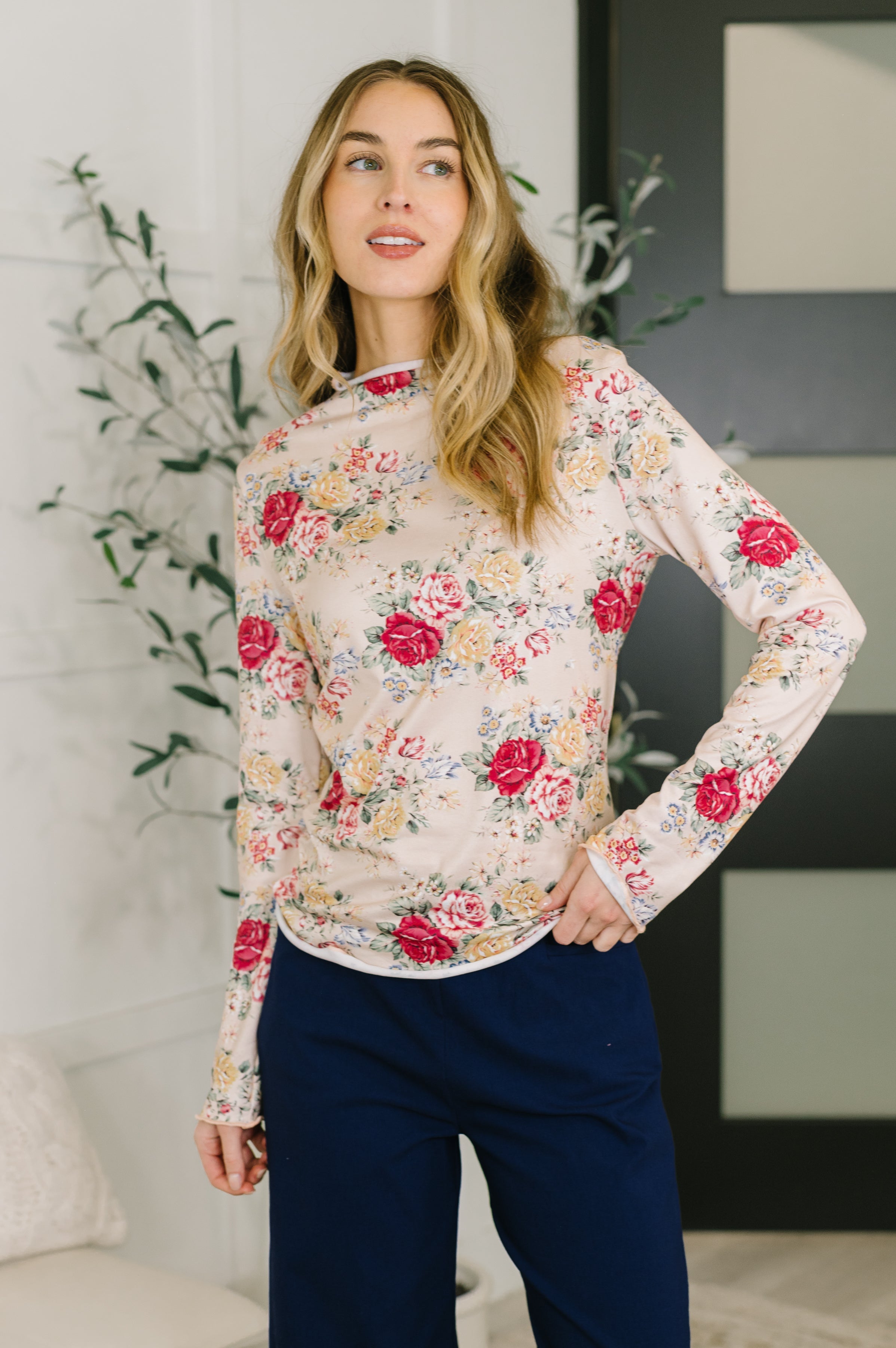 Woman wearing taupe long-sleeve top with high neck and red and yellow floral pattern paired with navy pants