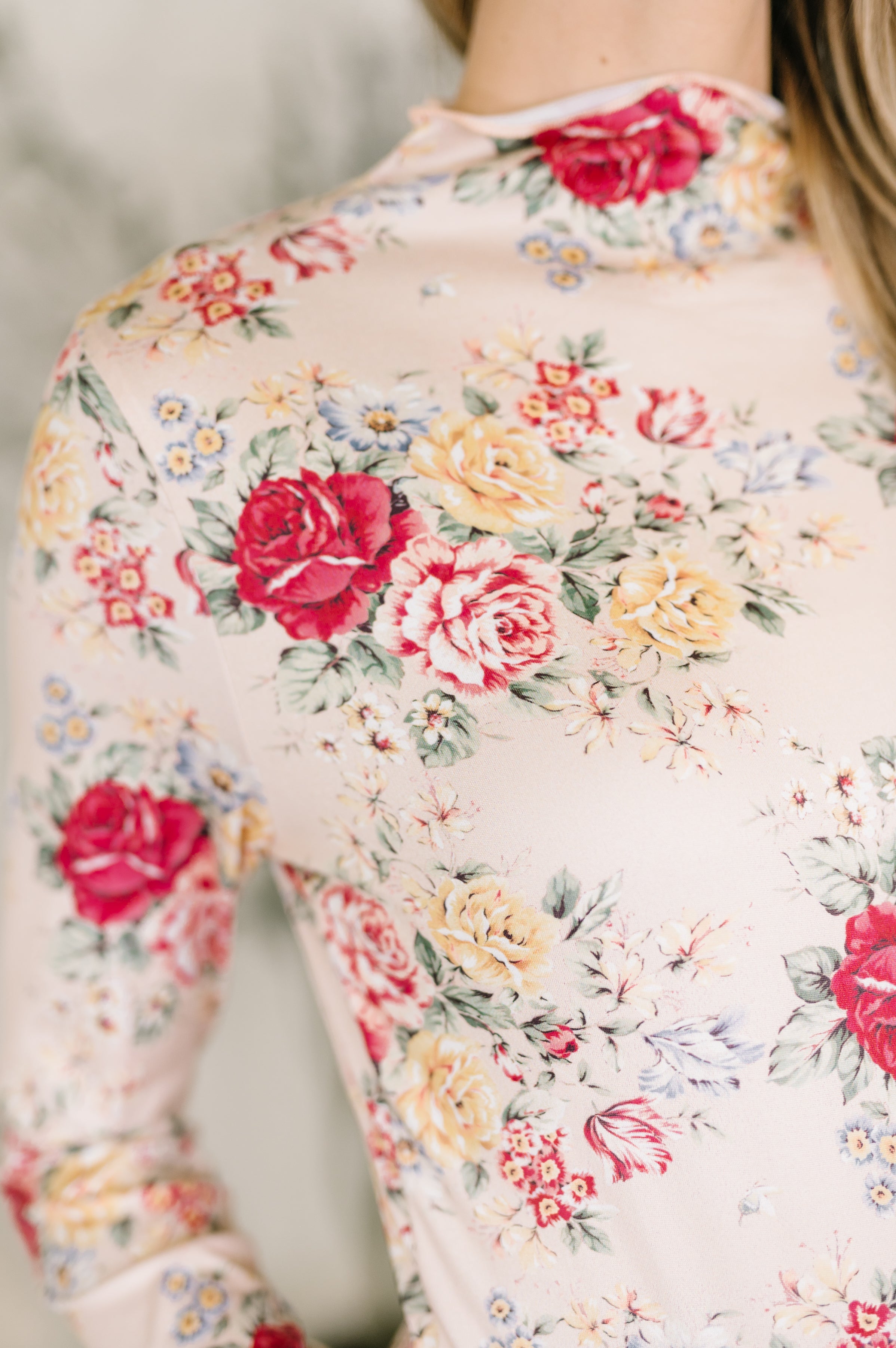 Close-up of taupe fabric with red, yellow, and cream floral print on a long-sleeve high-neck top