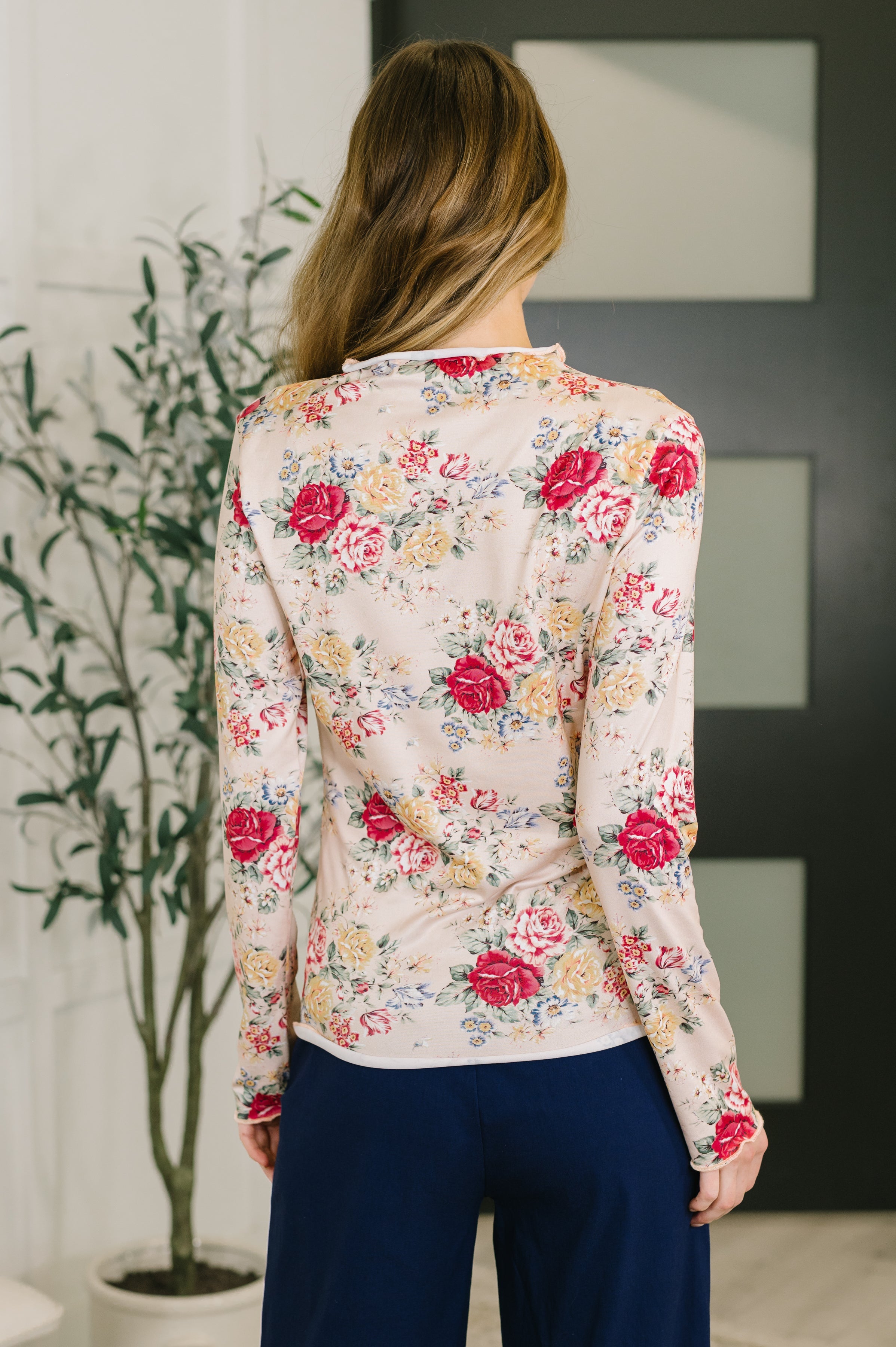 Woman wearing cream long-sleeve top with red, yellow, and blue floral print paired with navy trousers viewed from back