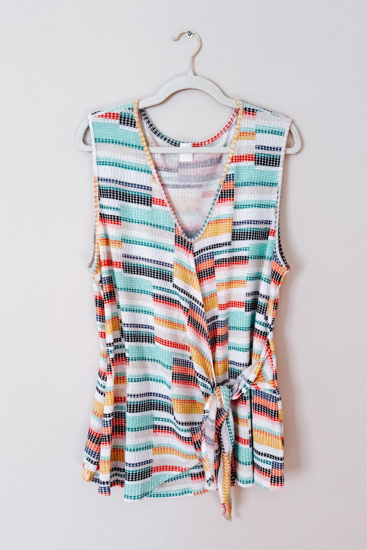 Blue multicolor striped V-neck knit tank with a faux wrap front and waist tie hanging on a hanger
