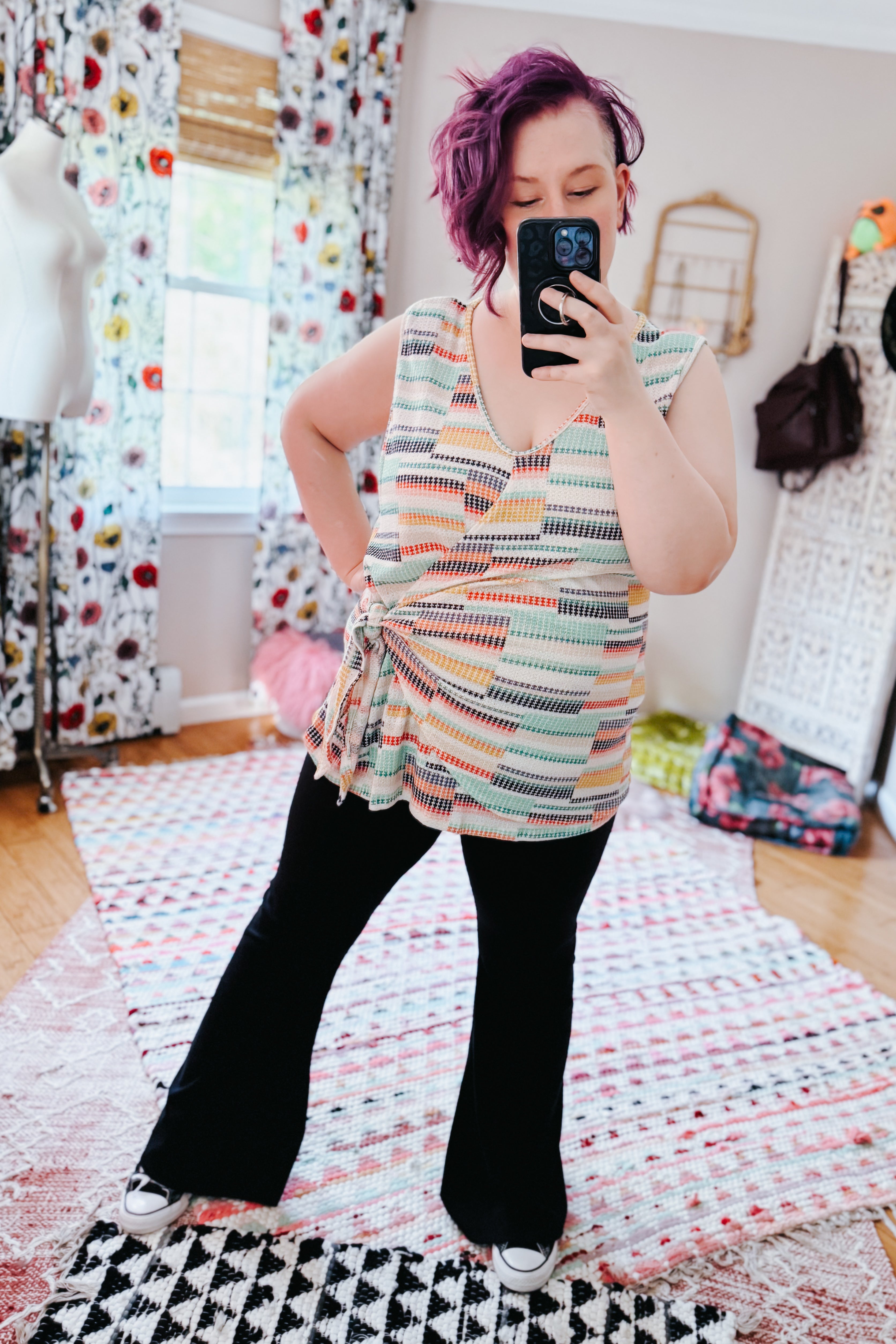 Woman wearing a colorful patterned wrap tank top paired with black wide-leg pants in a bright, eclectic room